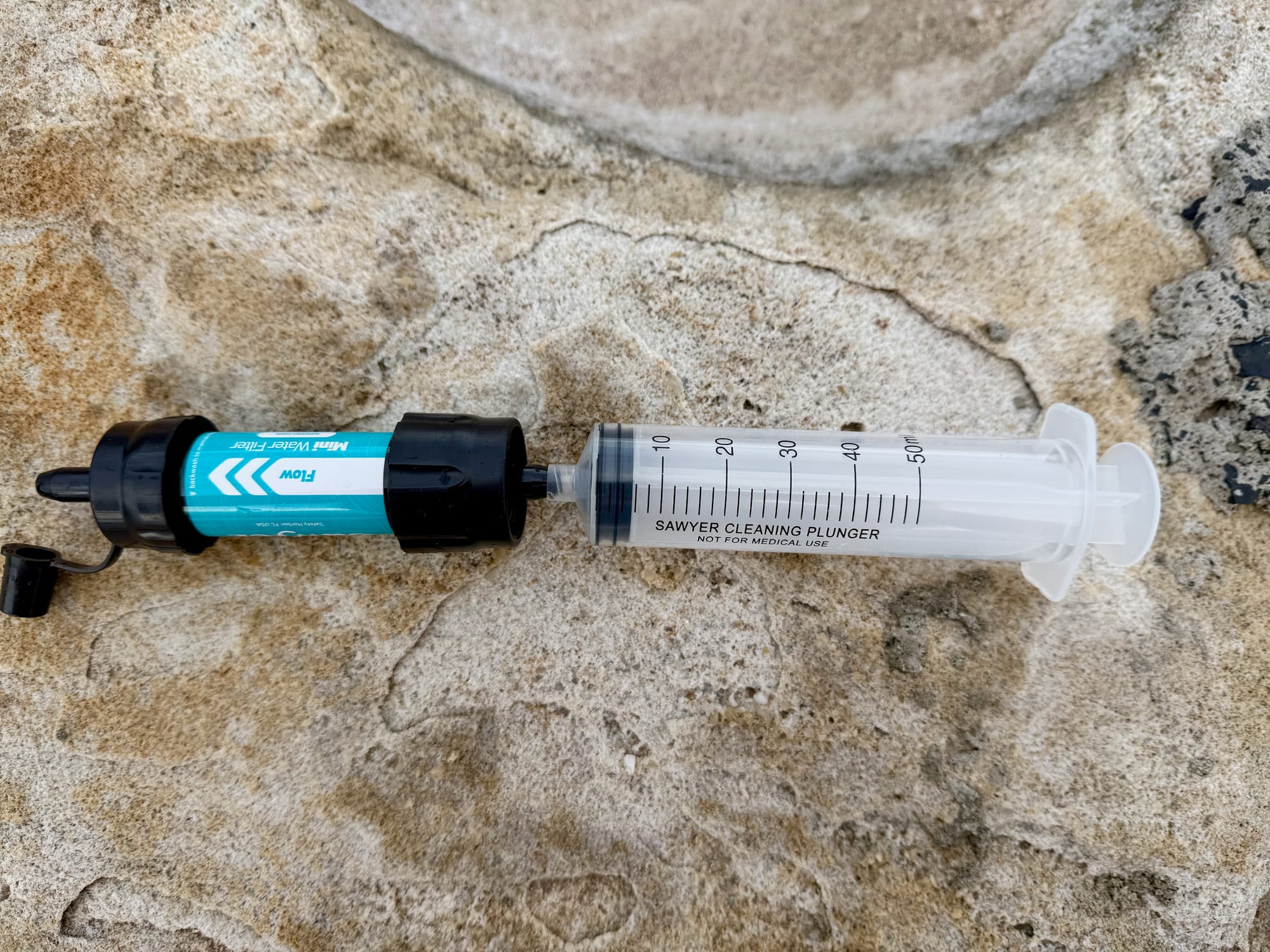 The Sawyer Mini with the cleaning plunger pushed onto its drinking end, lying on a sandstone rock