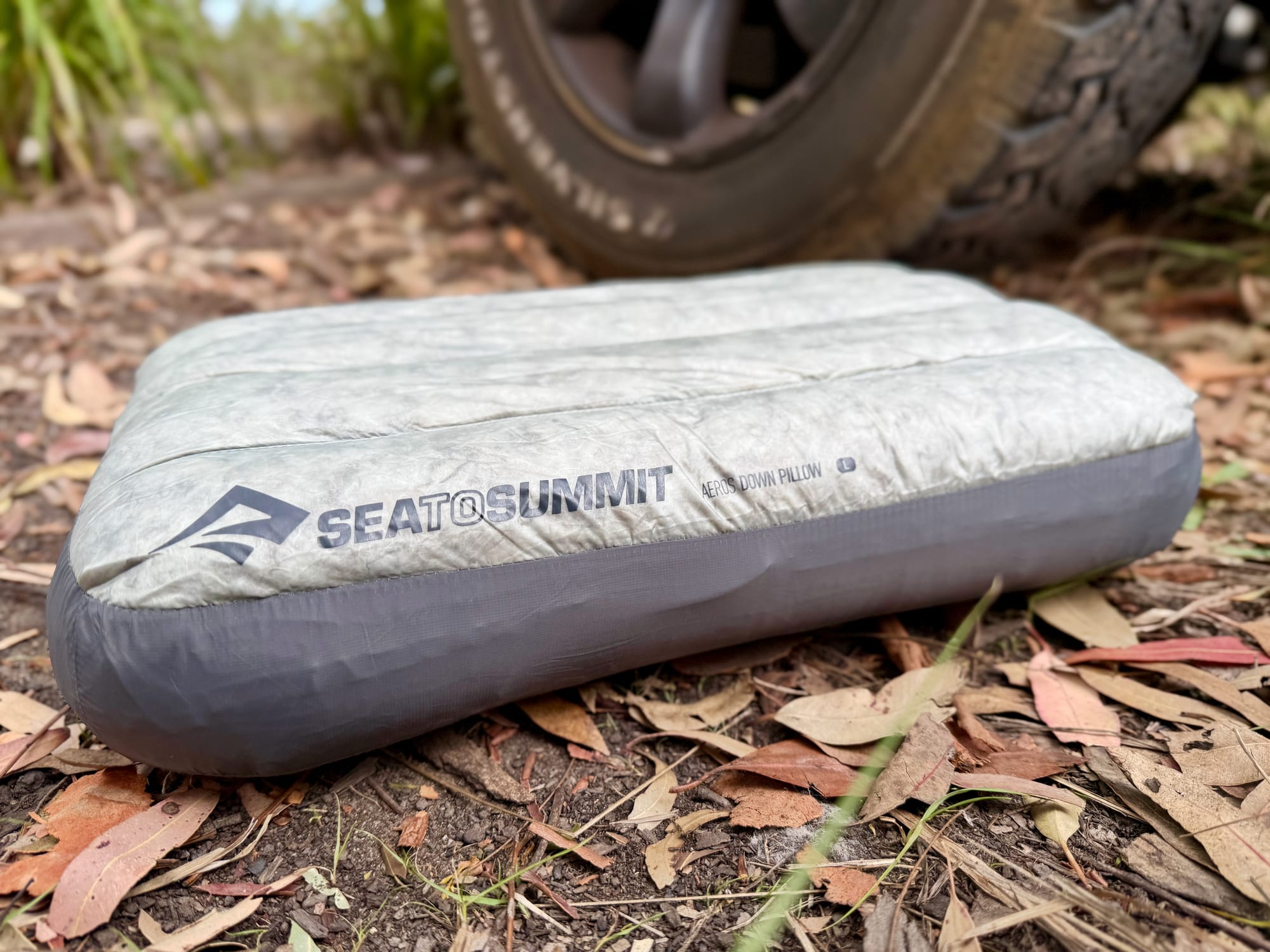 The Sea to Summit Aeros Down Pillow on the ground at camp, with the Prado’s wheel behind