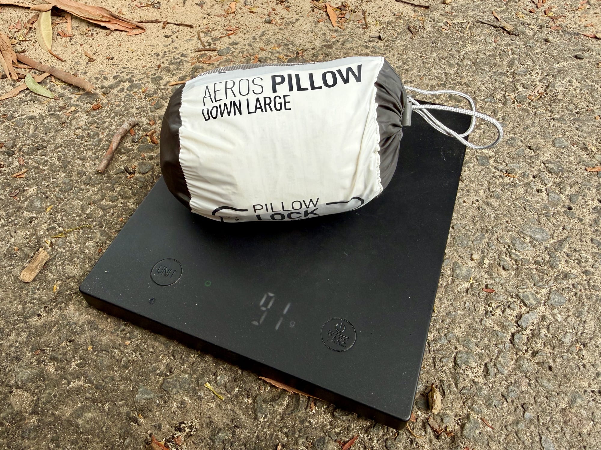 The Sea to Summit Aeros Down Pillow in its stuff sack on a scale showing 91 g