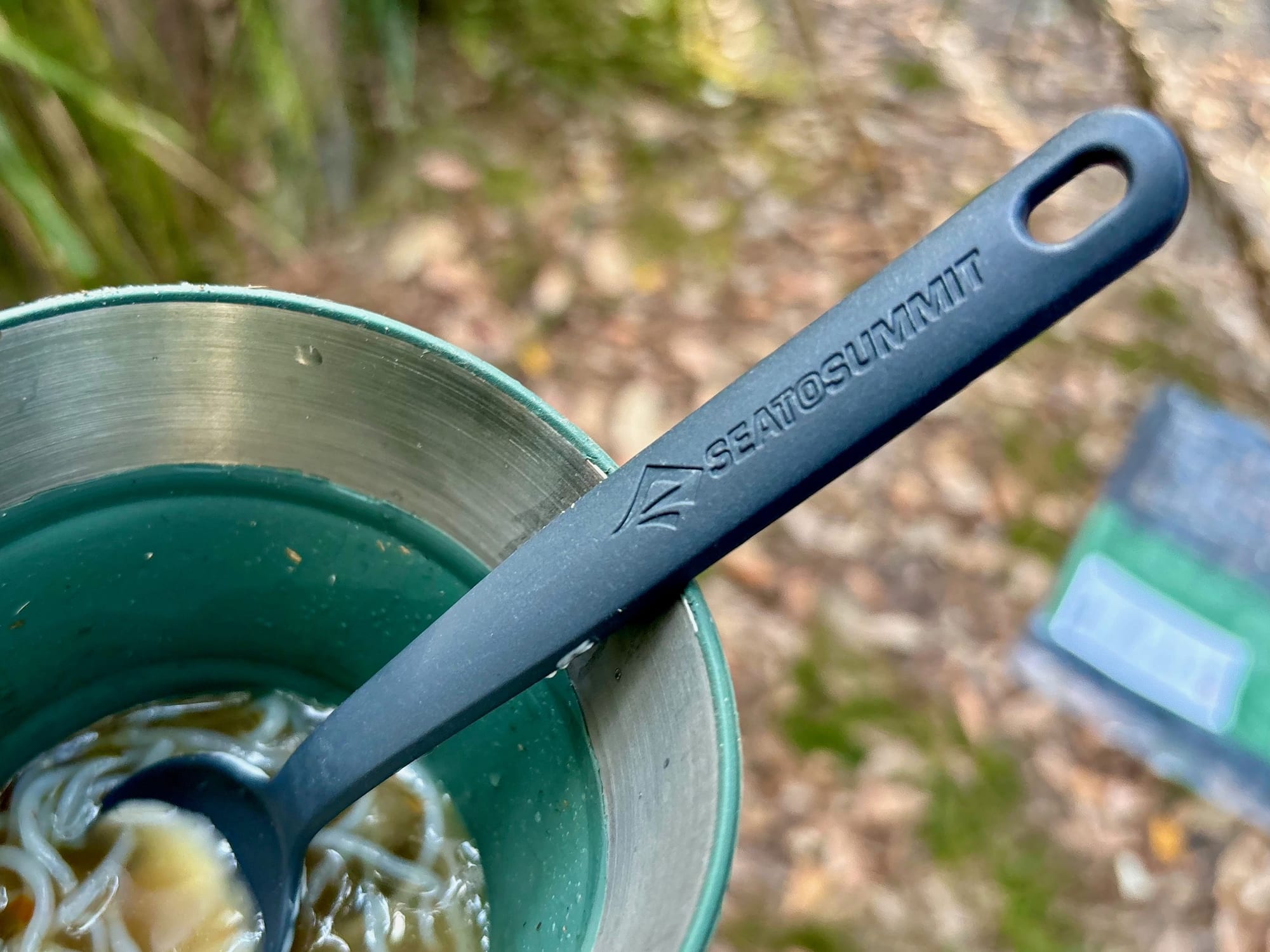 The Sea to Summit spork scooping noodle soup from a green collapsible mug