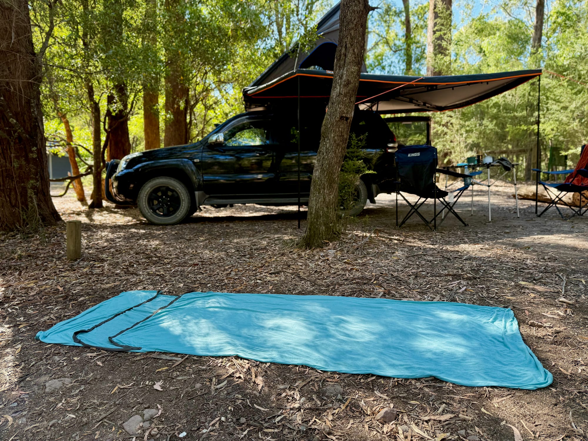 The Comfort Blend liner laid out flat at camp, rectangular from top to bottom, with our Prado and awning behind