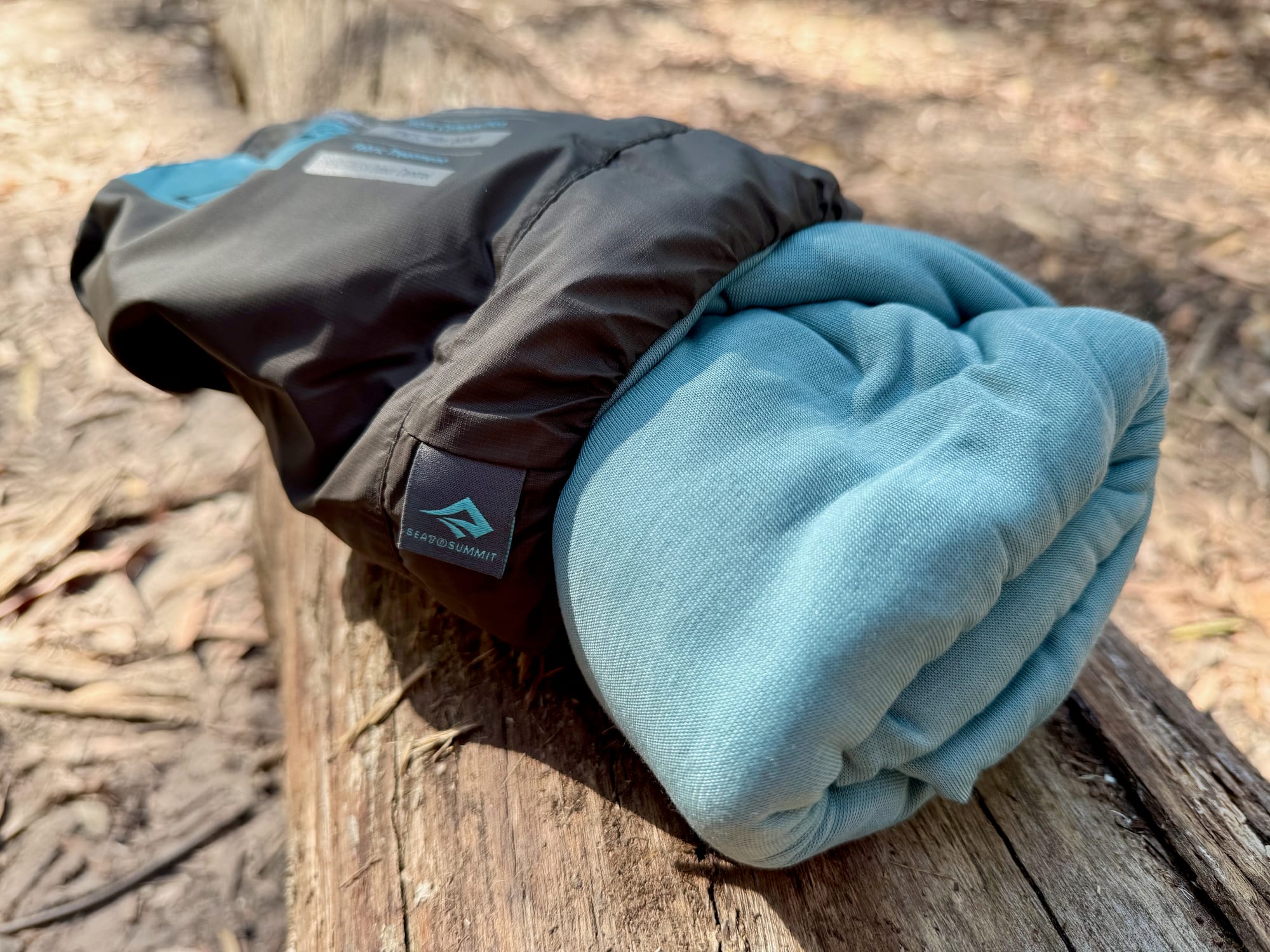 The Comfort Blend liner rolled up next to its stuff sack on a log