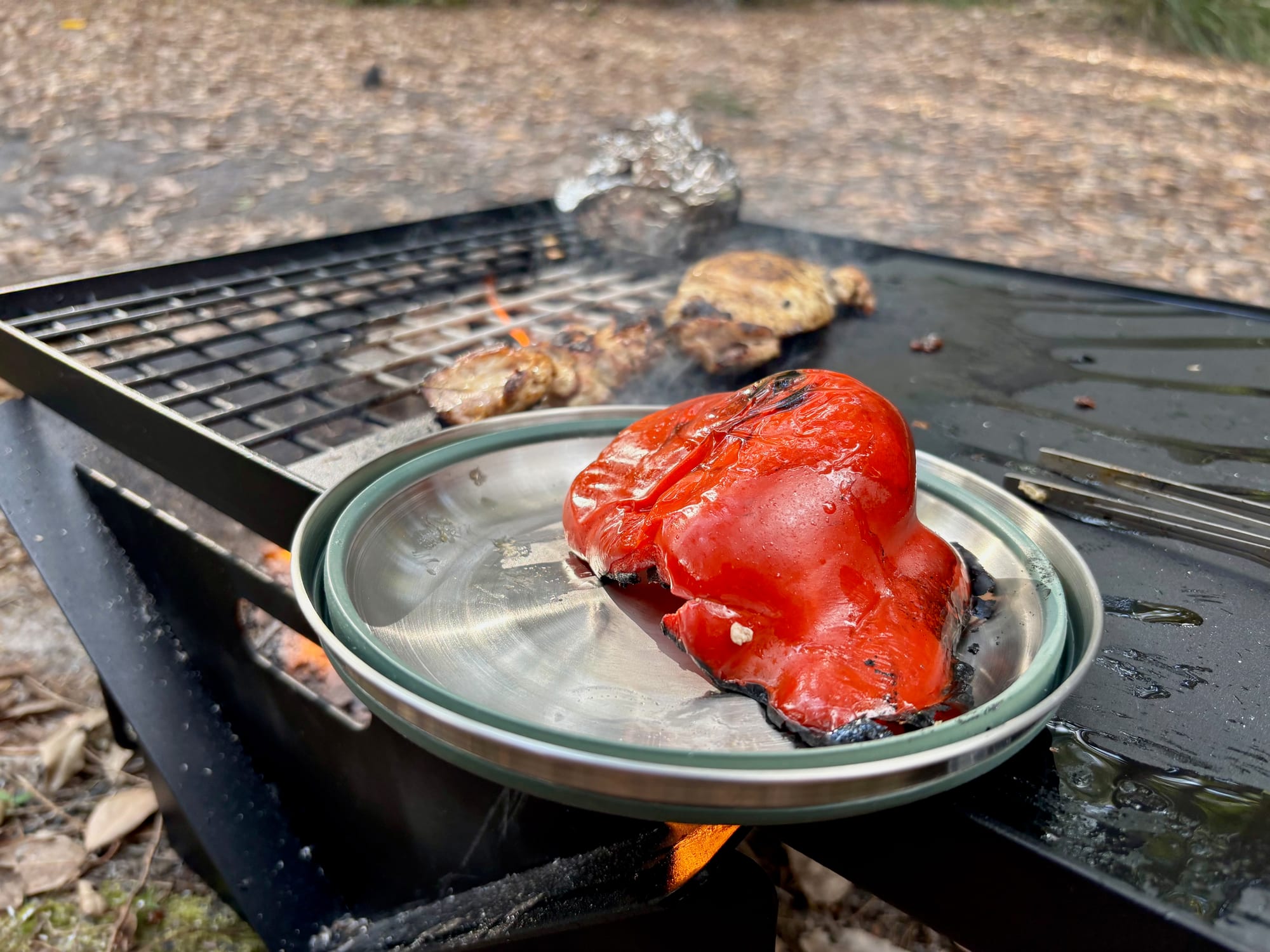 A collapsed green Detour bowl used as a plate with a grilled capsicum, on a fire grill
