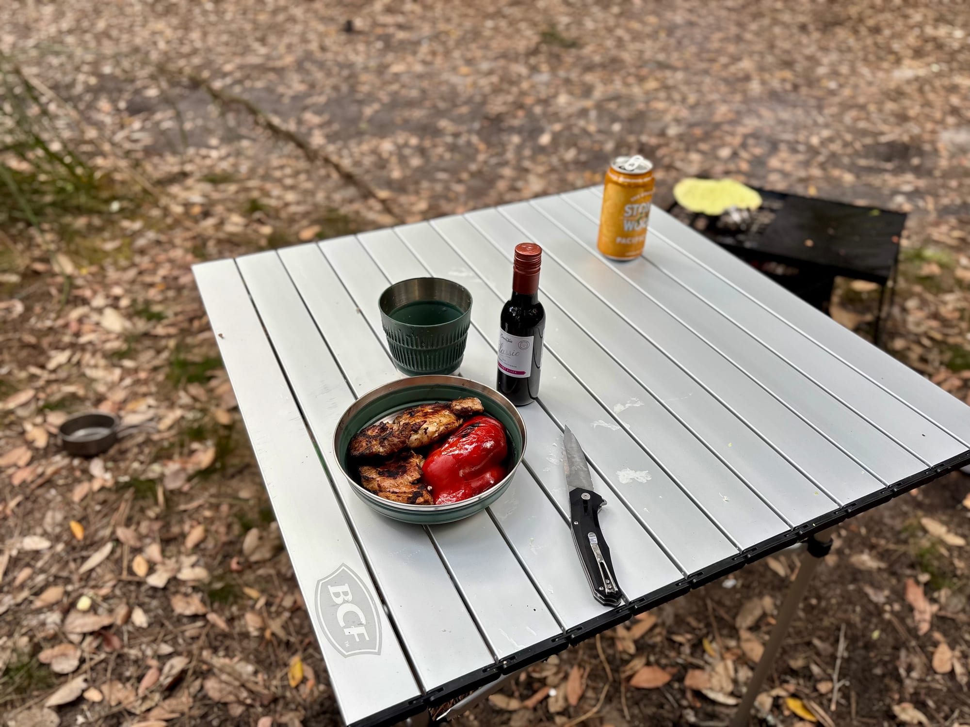 A Detour bowl with grilled meat and capsicum on a camp table, set with a Detour mug, wine and a knife