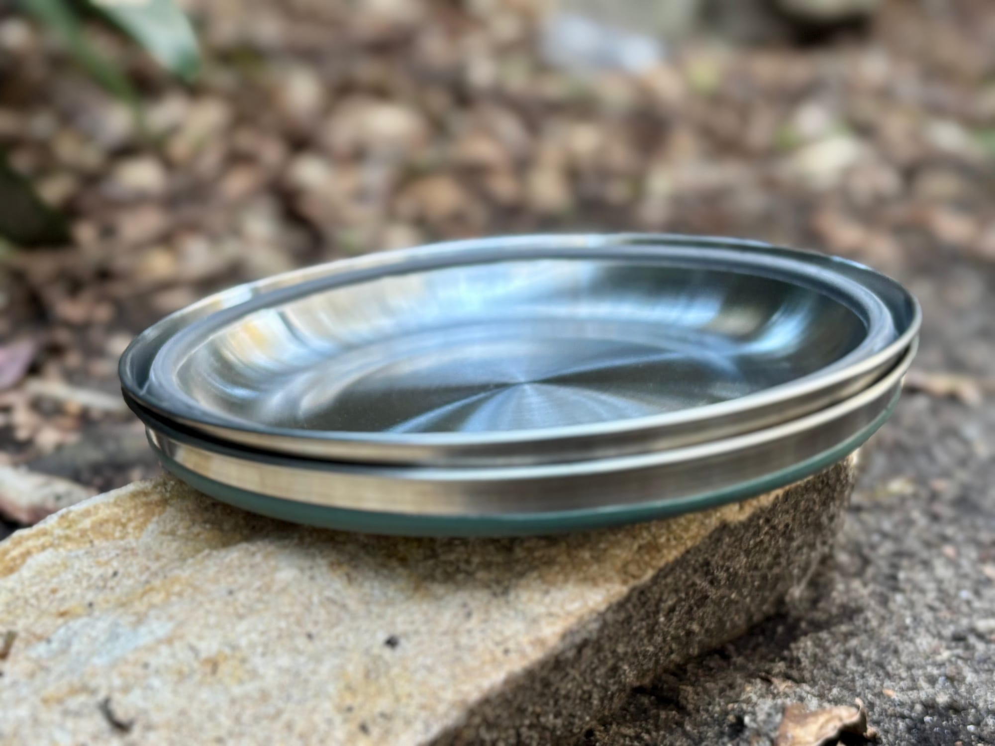 Two Detour bowls collapsed and stacked on a rock, one green and one charcoal