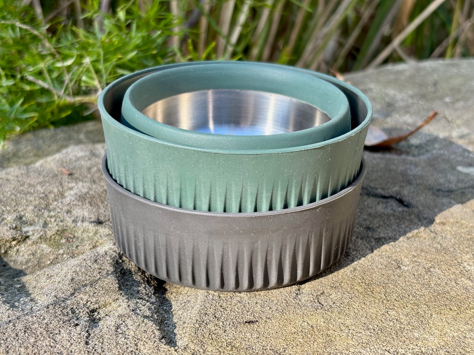 A collapsed green Detour mug nested on a collapsed charcoal Detour bowl on a rock
