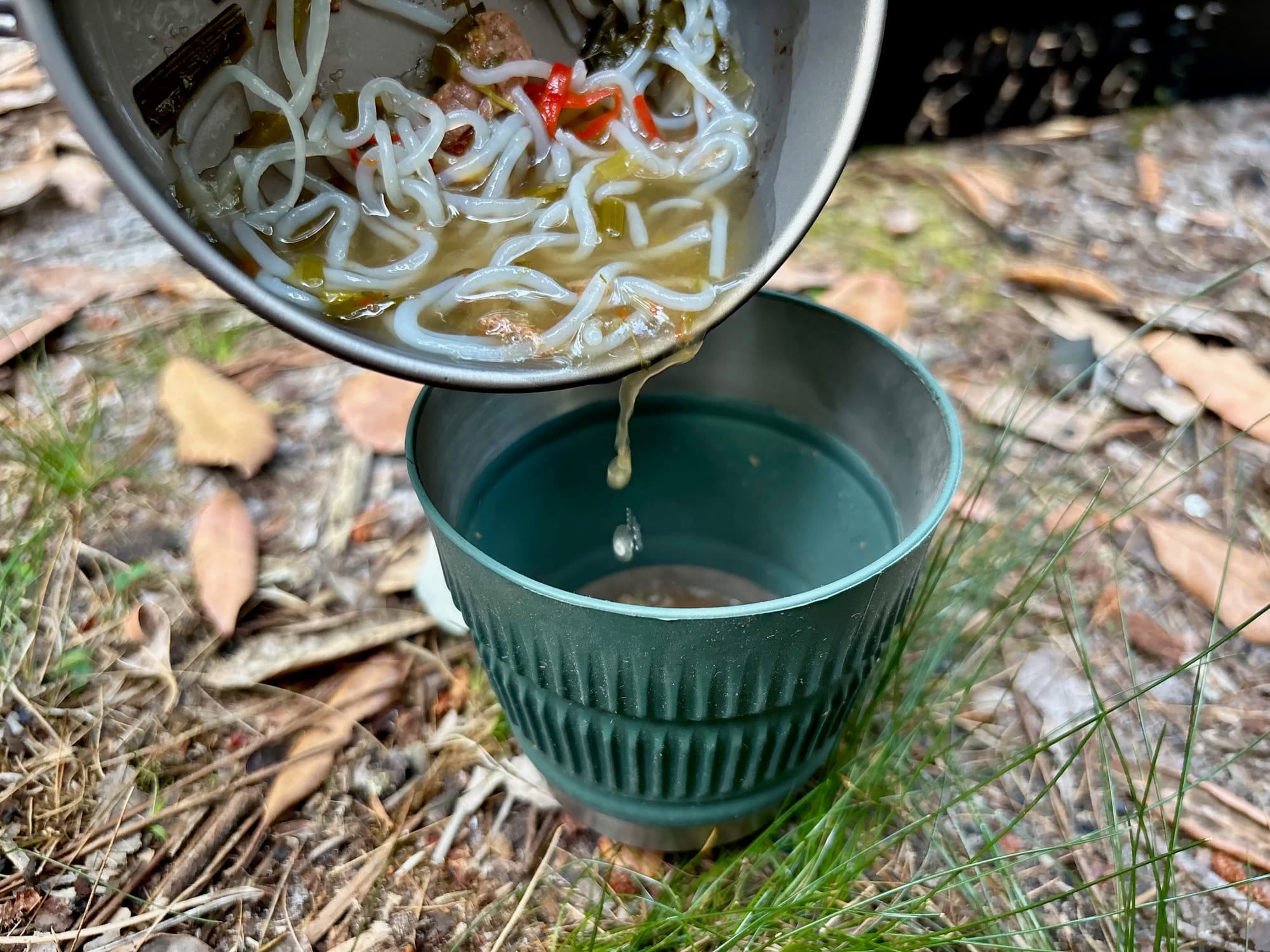 Noodle soup being poured from a camping pot into the green Detour collapsible mug
