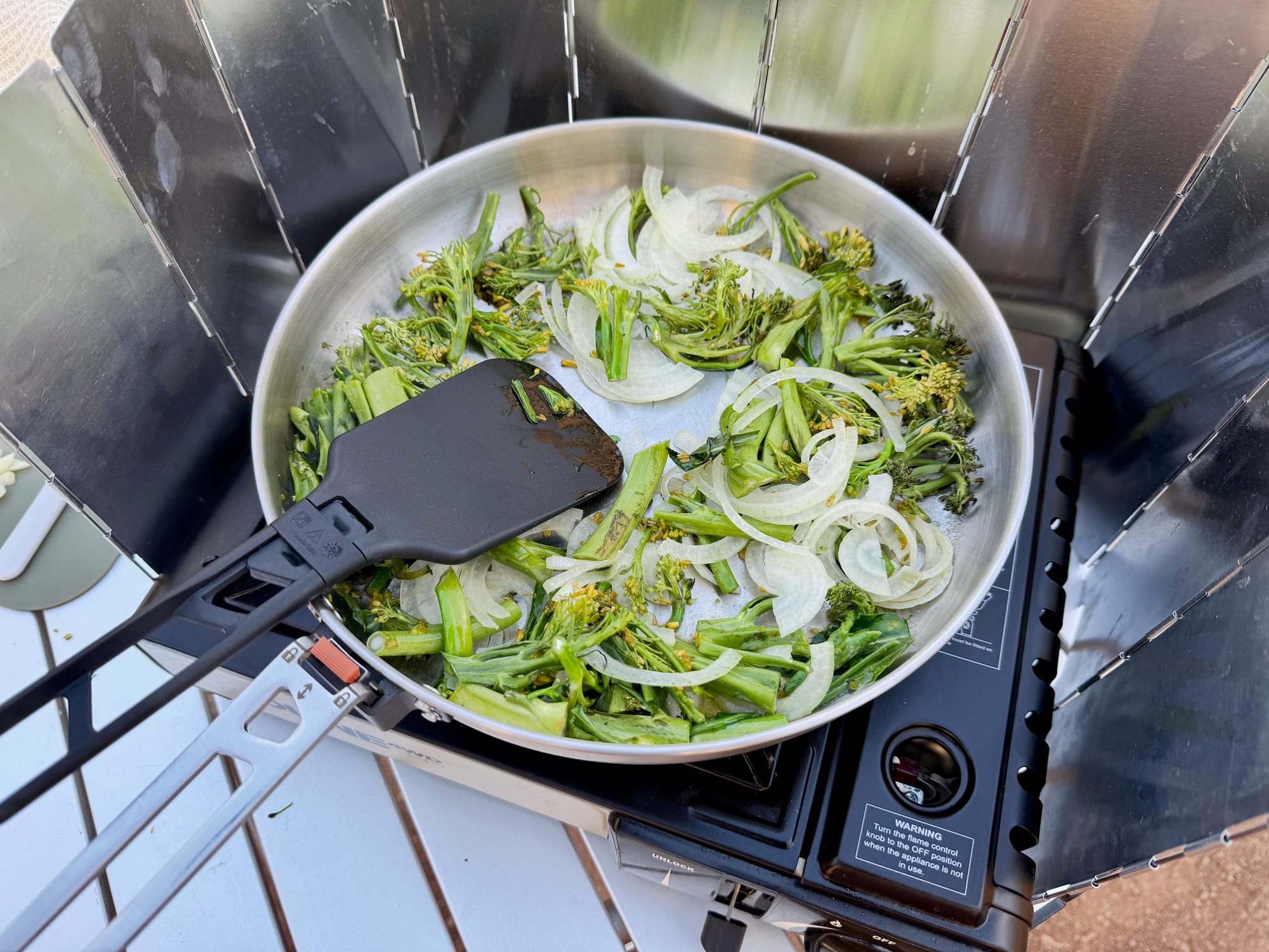 Onion and broccolini frying in the Sea to Summit Detour Pan with a black spatula