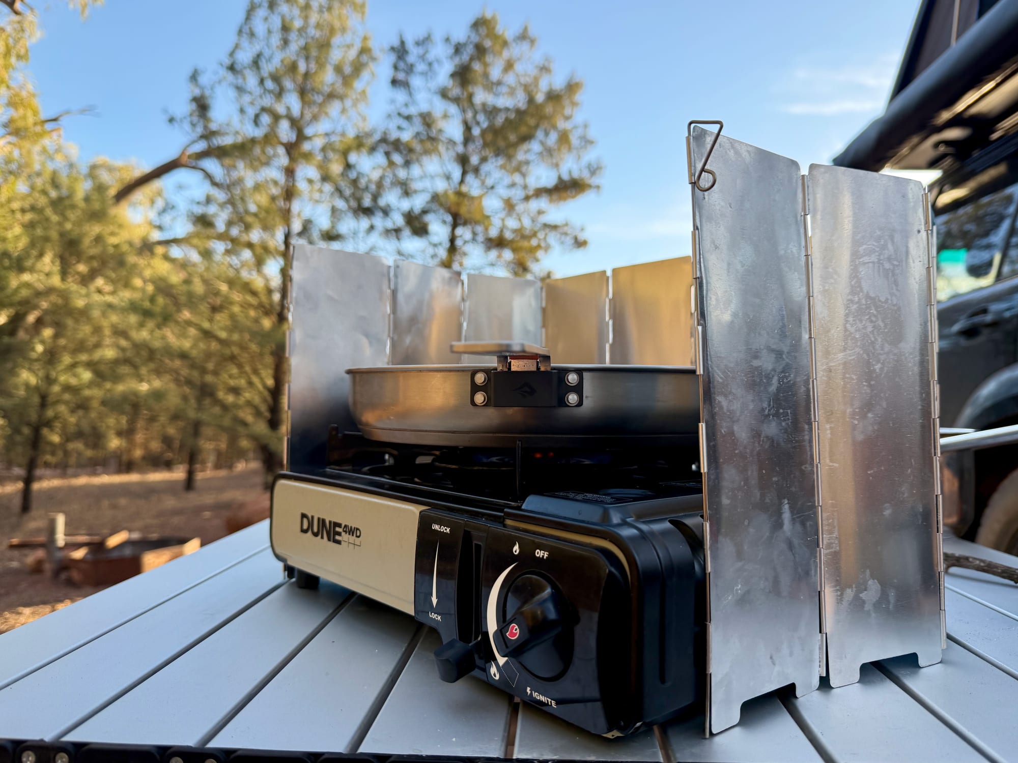 The Sea to Summit Detour Pan on a Dune single burner butane stove behind a foil windscreen, next to the Prado