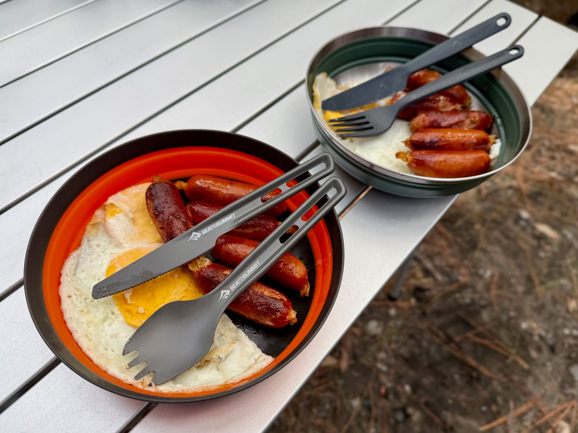 An orange Frontier bowl with eggs and sausages next to a green Detour bowl with sausages