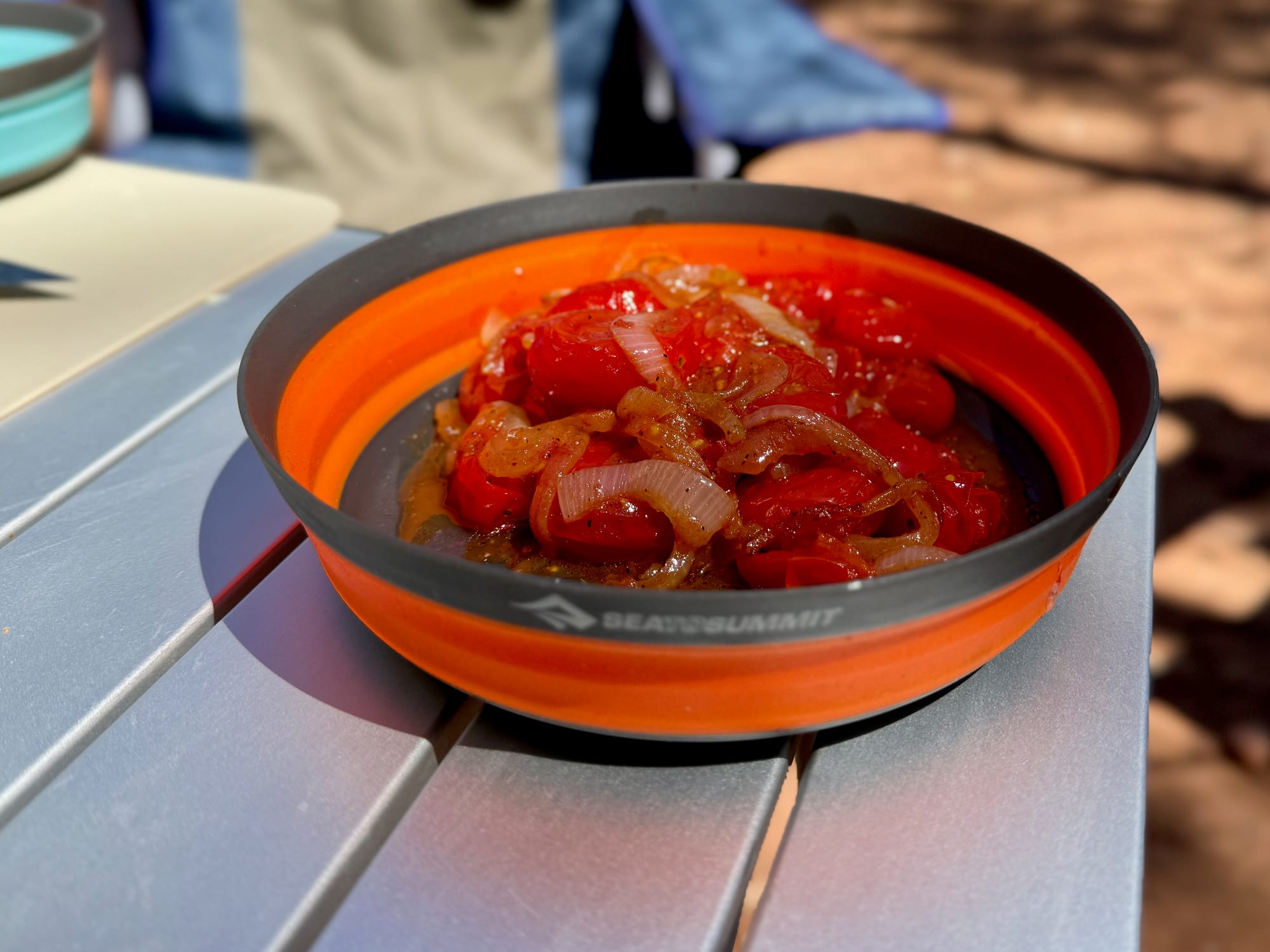 The Large orange Frontier bowl with cooked tomatoes and onion on a camp table
