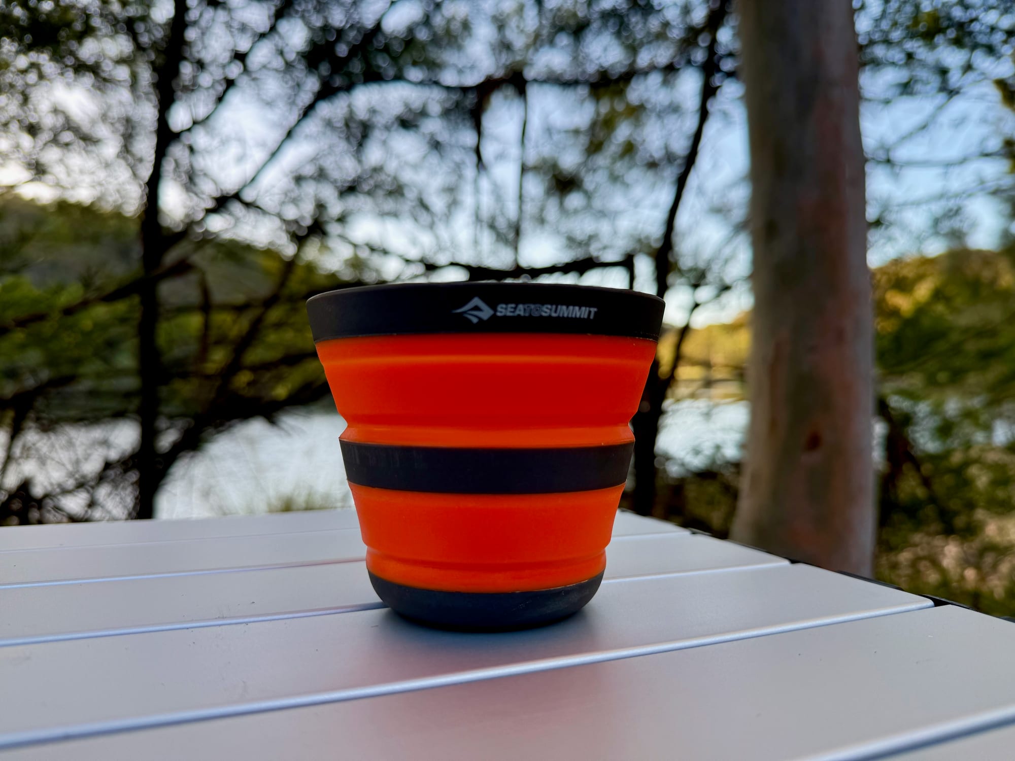 The Frontier collapsible cup open on an aluminium camp table by a lake