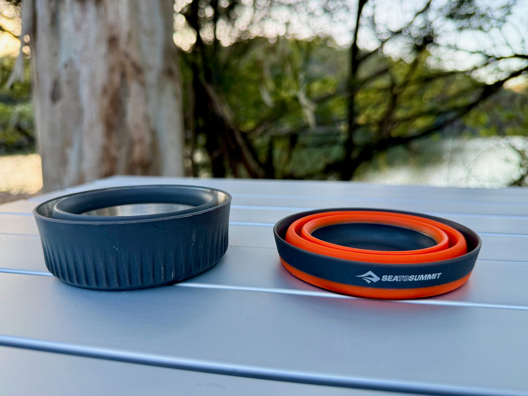 The collapsed Frontier cup next to the collapsed Detour mug on a camp table
