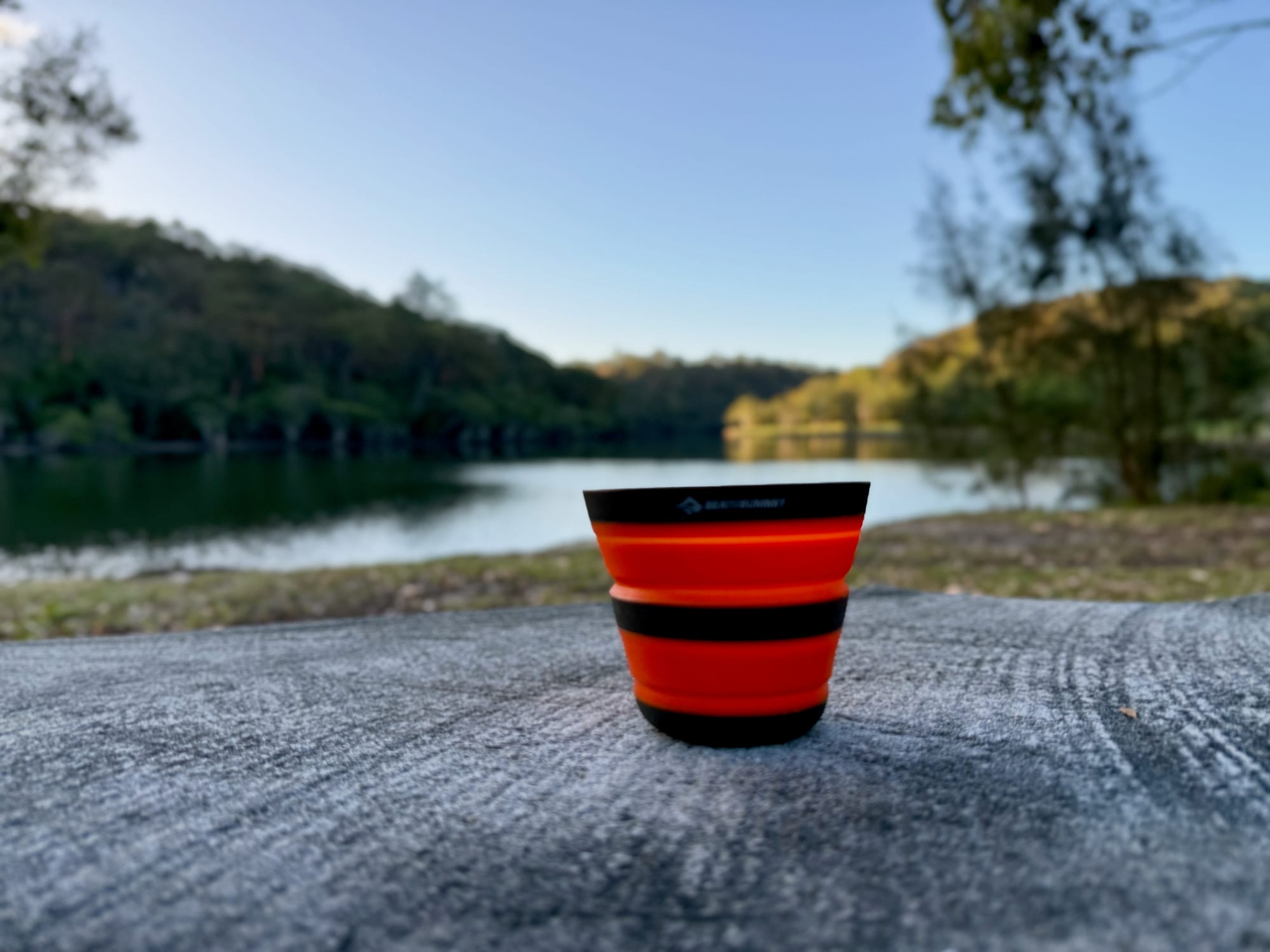 The Frontier collapsible cup open on a log by a lake