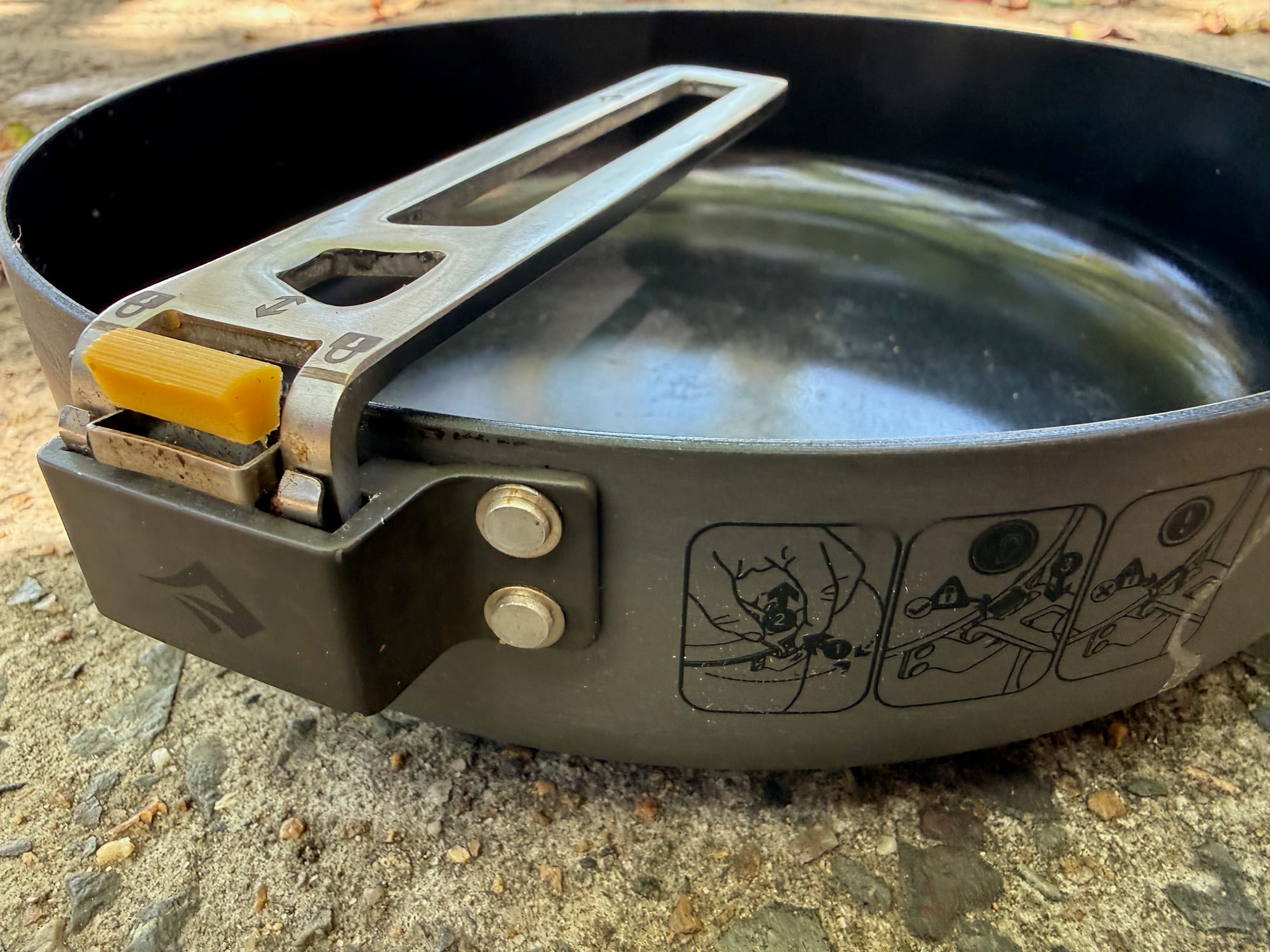 A close-up of the Click-Safe handle on the Frontier Ultralight Pan, with its yellow tab and the metal bracket on the side of the pan