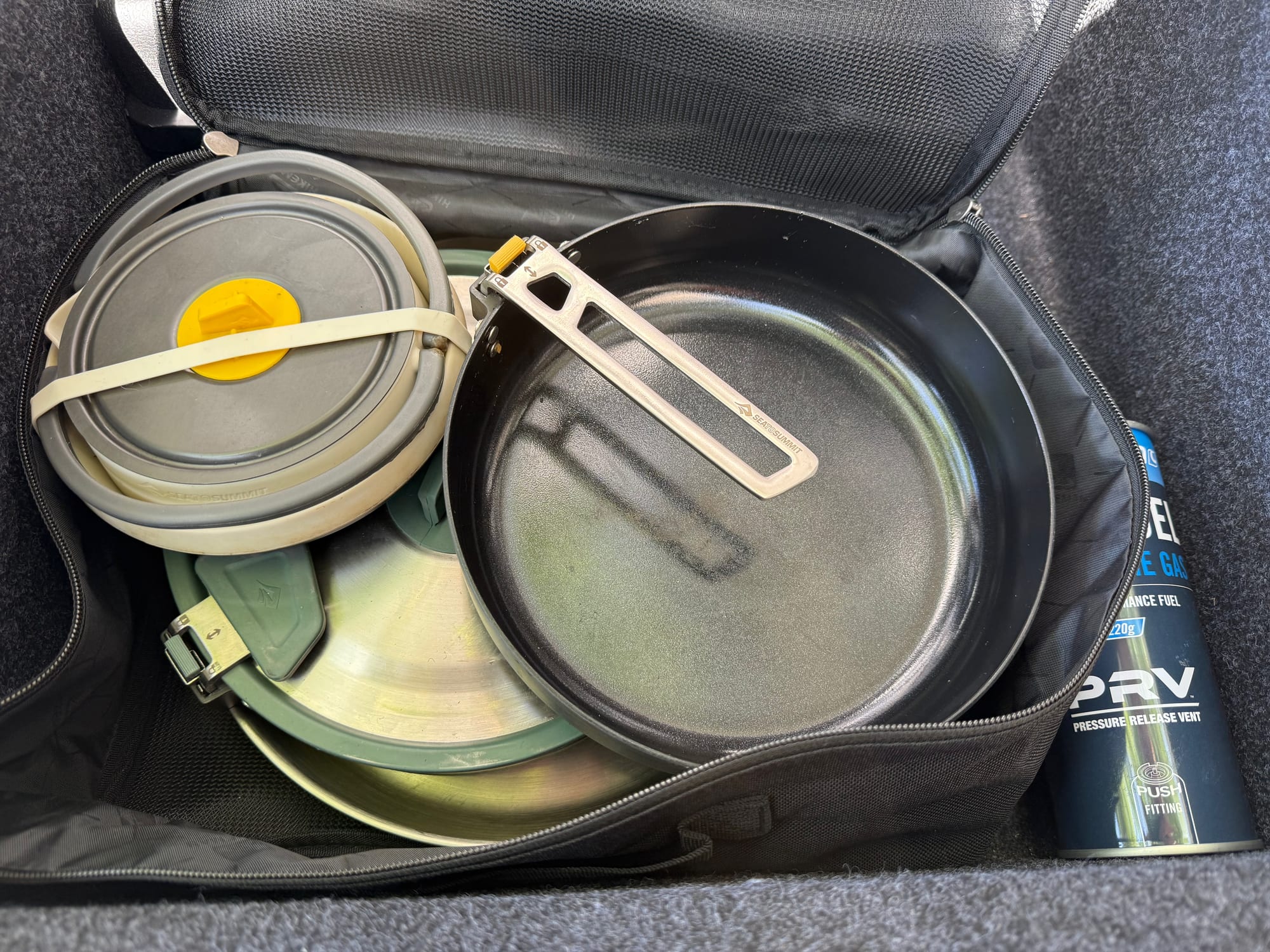 The Frontier Ultralight Pan in an open zip-up bag in the back of the car, next to a collapsed pot and a stainless steel pan