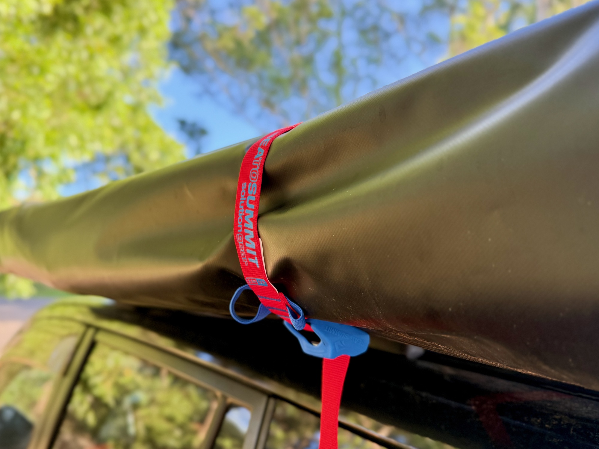 A red Sea to Summit tie down wrapped around the awning bag on the roof rack, with its blue cam cover hanging below