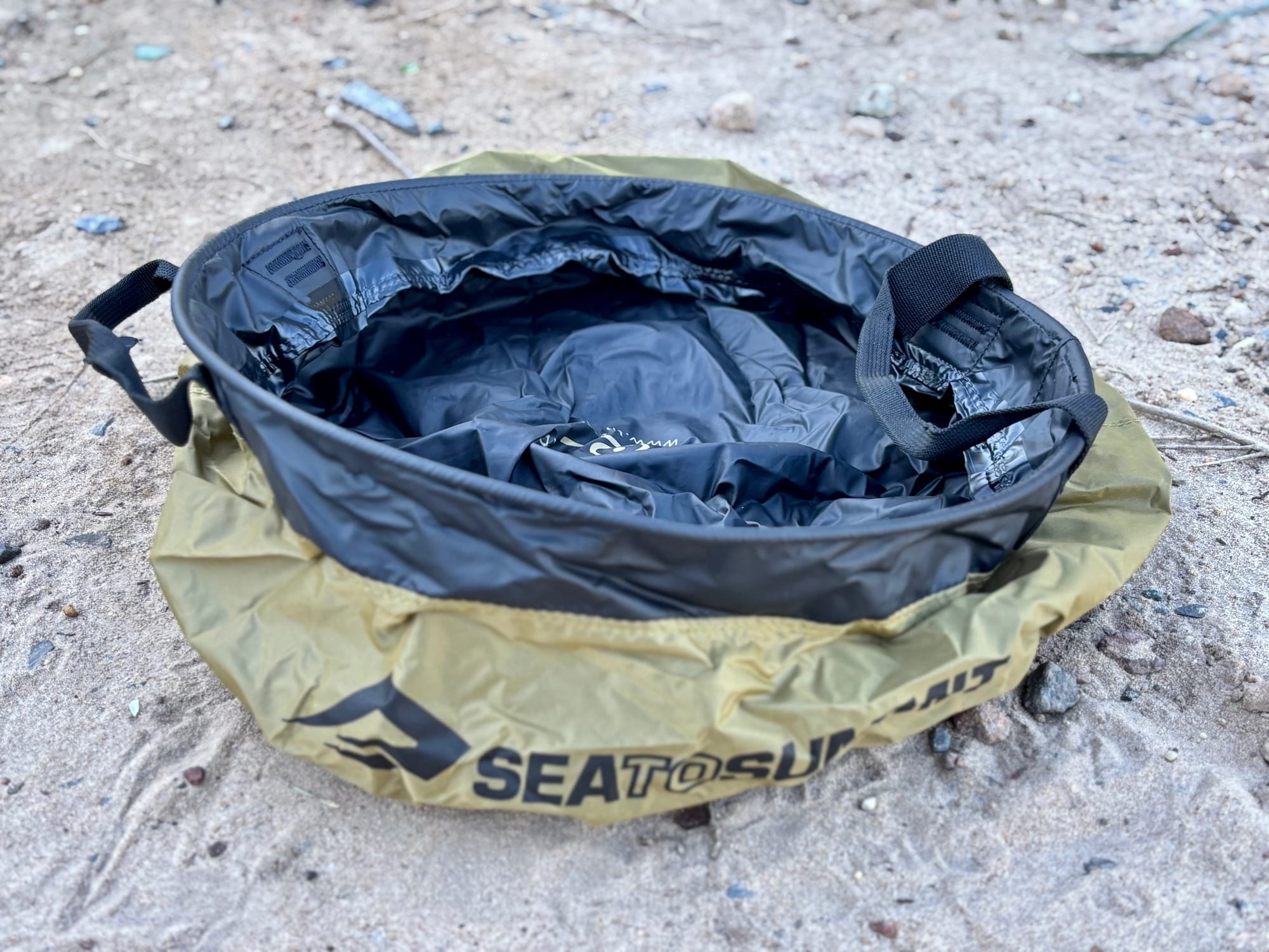 The Sea to Summit Kitchen Sink half unfolded on sandy ground