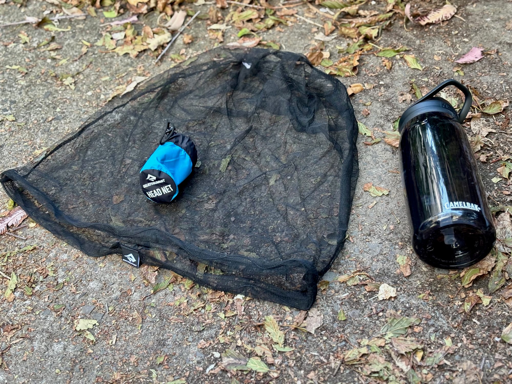 The Sea to Summit Head Net spread out flat on the ground, with its stuff sack on top and a water bottle beside it