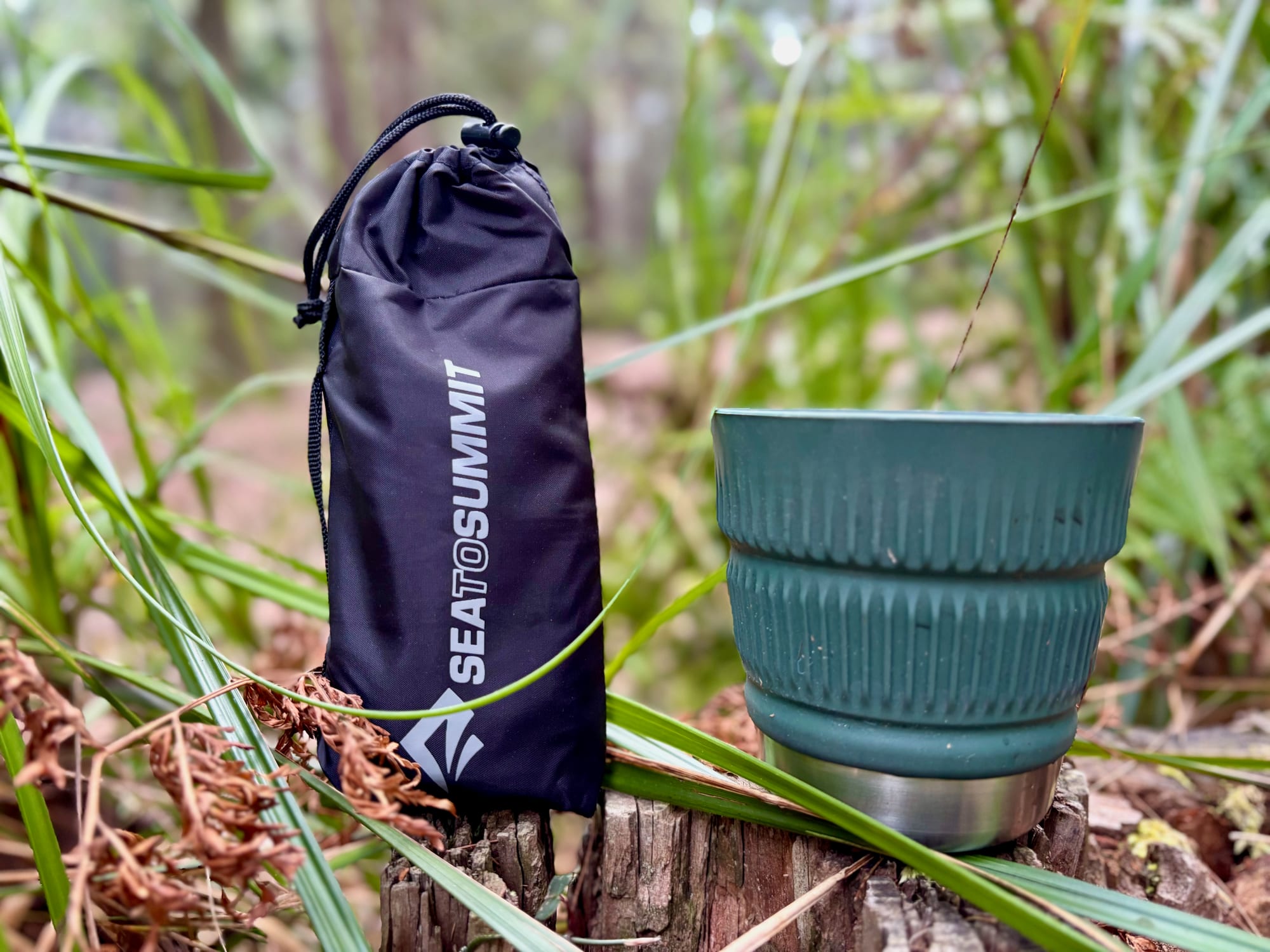 The Sea to Summit Pocket Umbrella in its pouch, standing next to a camp mug