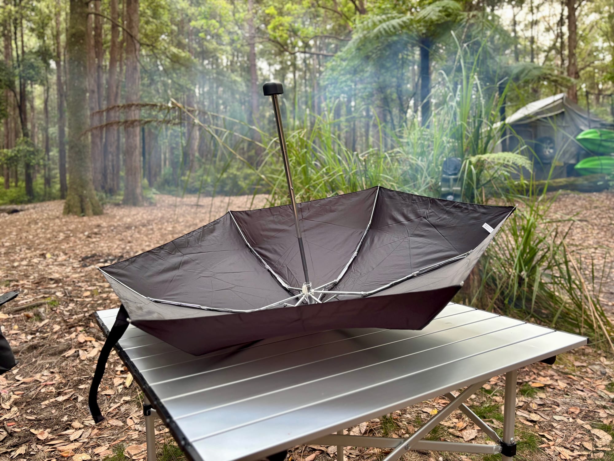 The Sea to Summit Pocket Umbrella open upside down on a 70 × 70 cm camp table, showing the shaft and handle