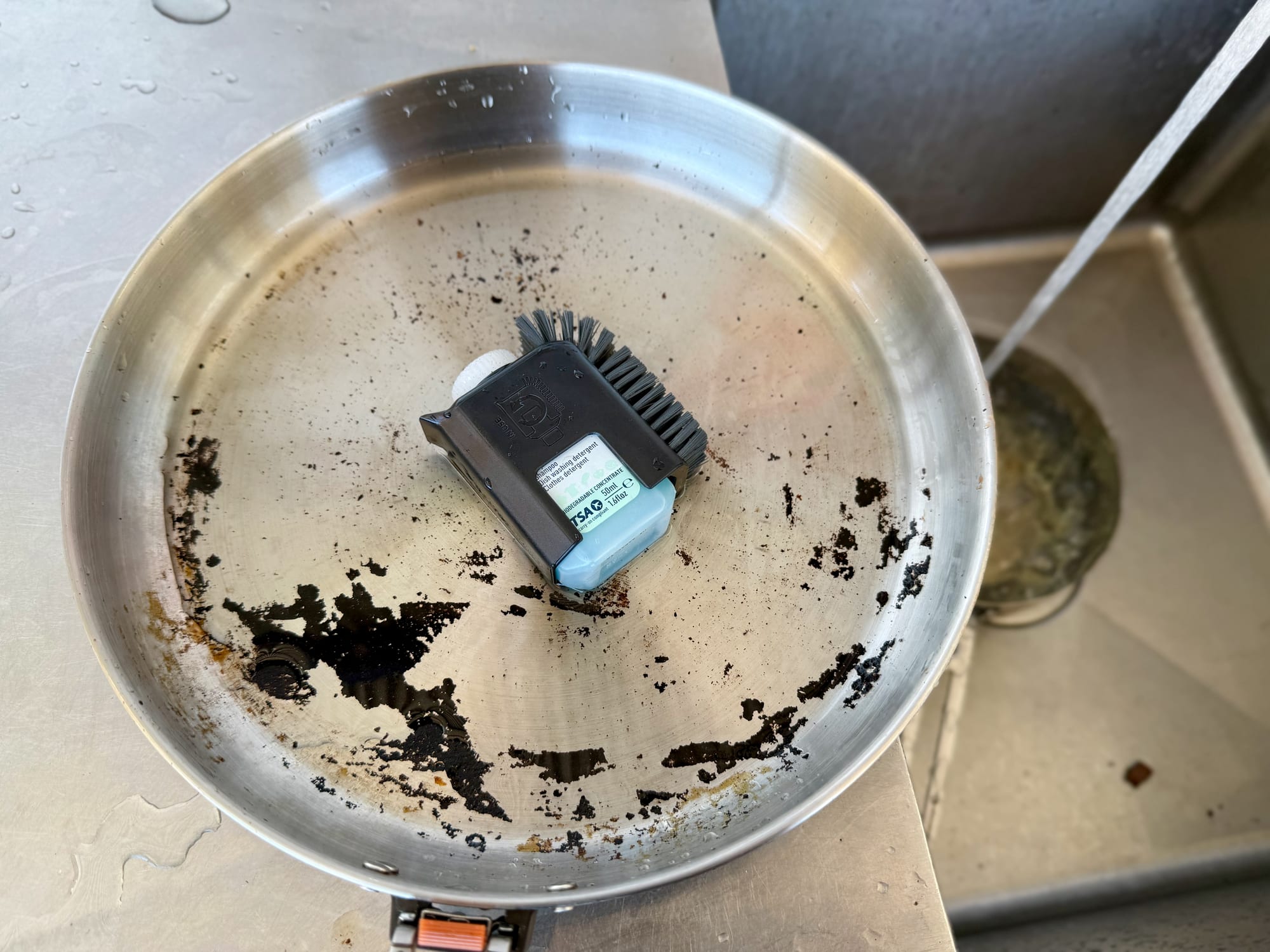 The Sea to Summit Pot Scrubber lying in the Sea to Summit Detour stainless steel pan with burnt-on egg