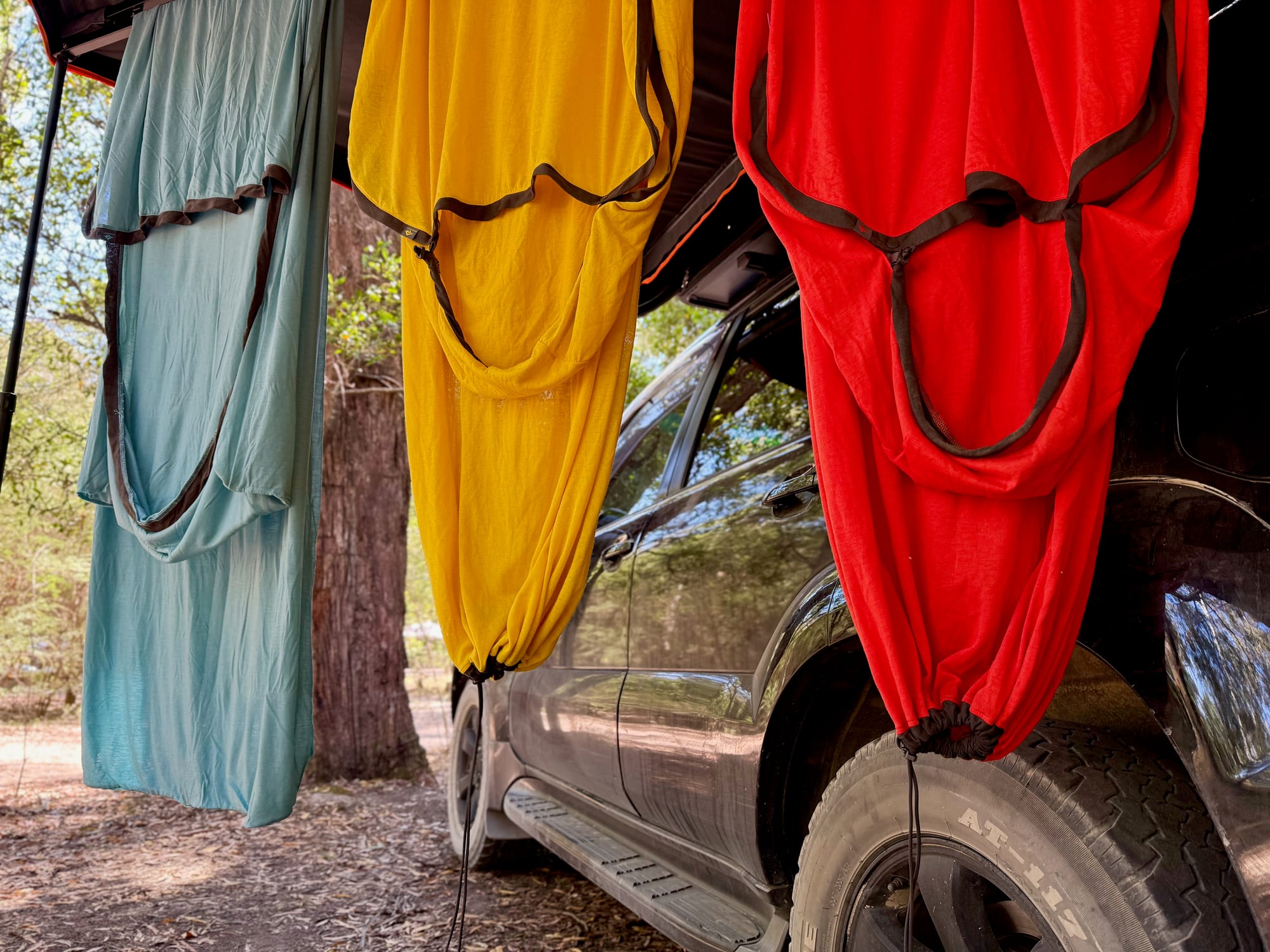 The red Reactor Extreme liner hanging under the awning beside the Reactor Lightweight and Comfort Blend, with its hood at the top and the footbox drawcord at the bottom