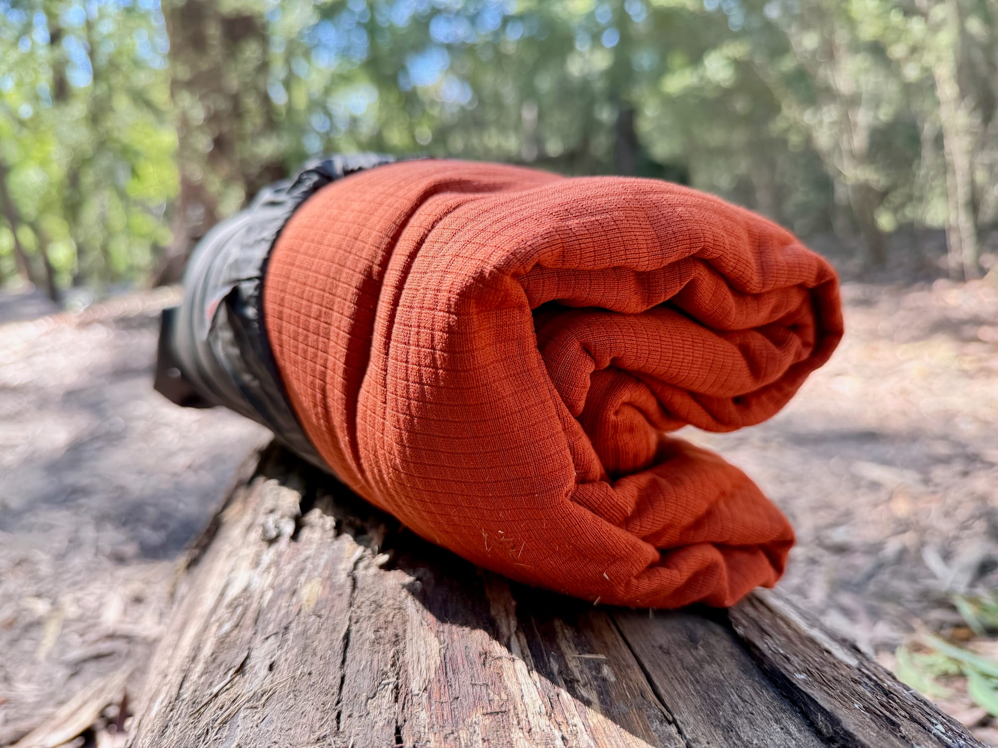 The rust-orange grid fleece of the Reactor Fleece liner, folded out of its stuff sack on a log