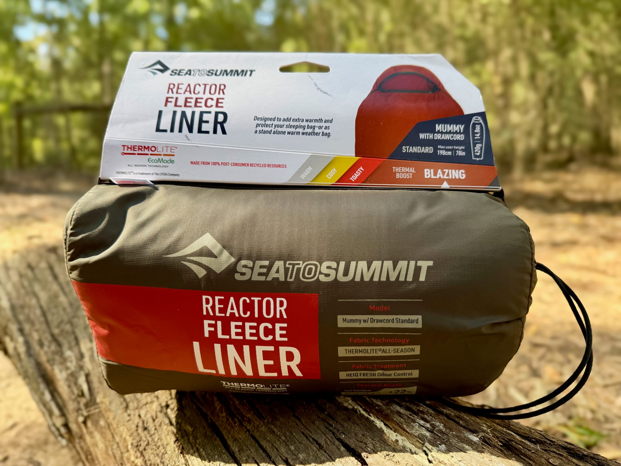 The Sea to Summit Reactor Fleece liner in its box and grey stuff sack on a log