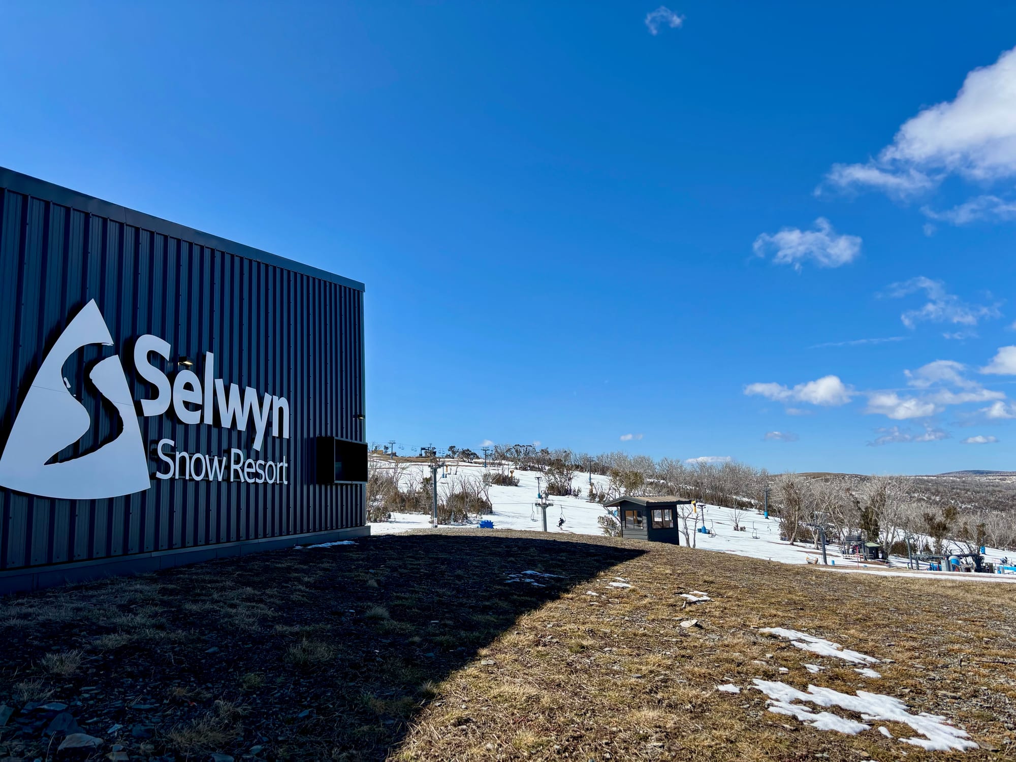 The Selwyn Snow Resort sign on the building, with the slopes and lifts behind