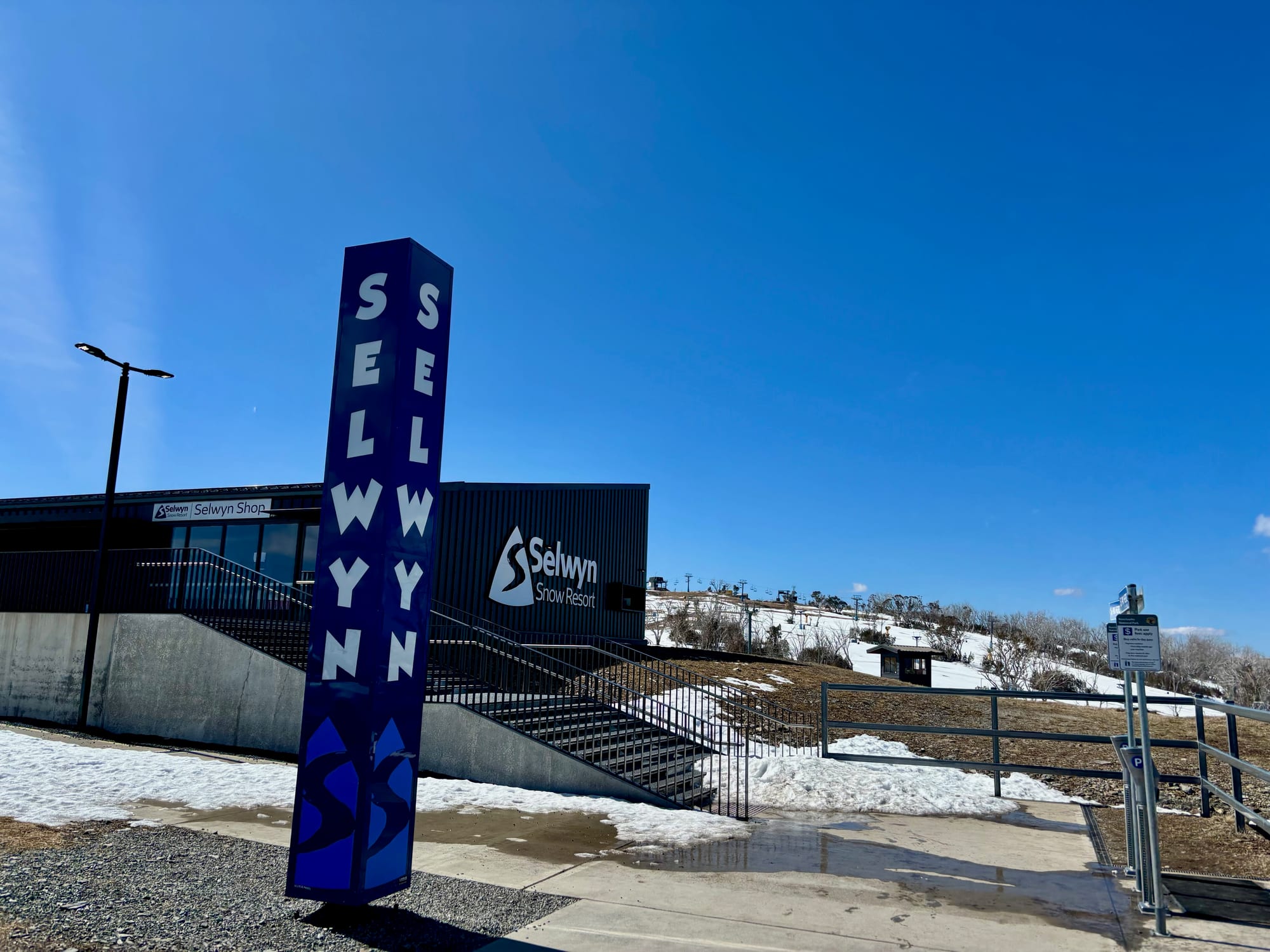 The blue Selwyn pylon in front of the main building, with the Selwyn Shop sign and steps up from the car park