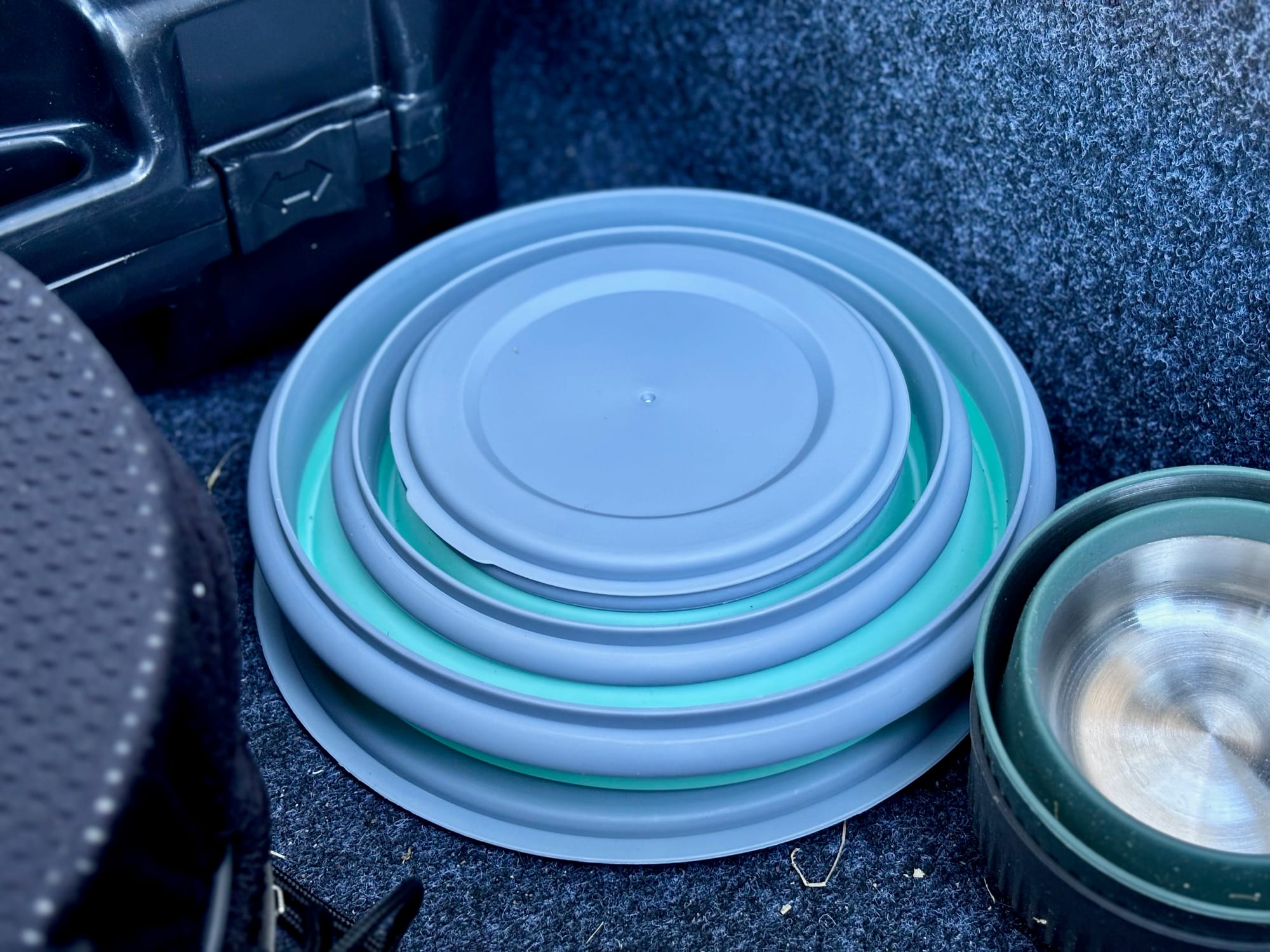 The three silicone bowls folded flat and nested into one stack with their lids, in the back of a 4WD