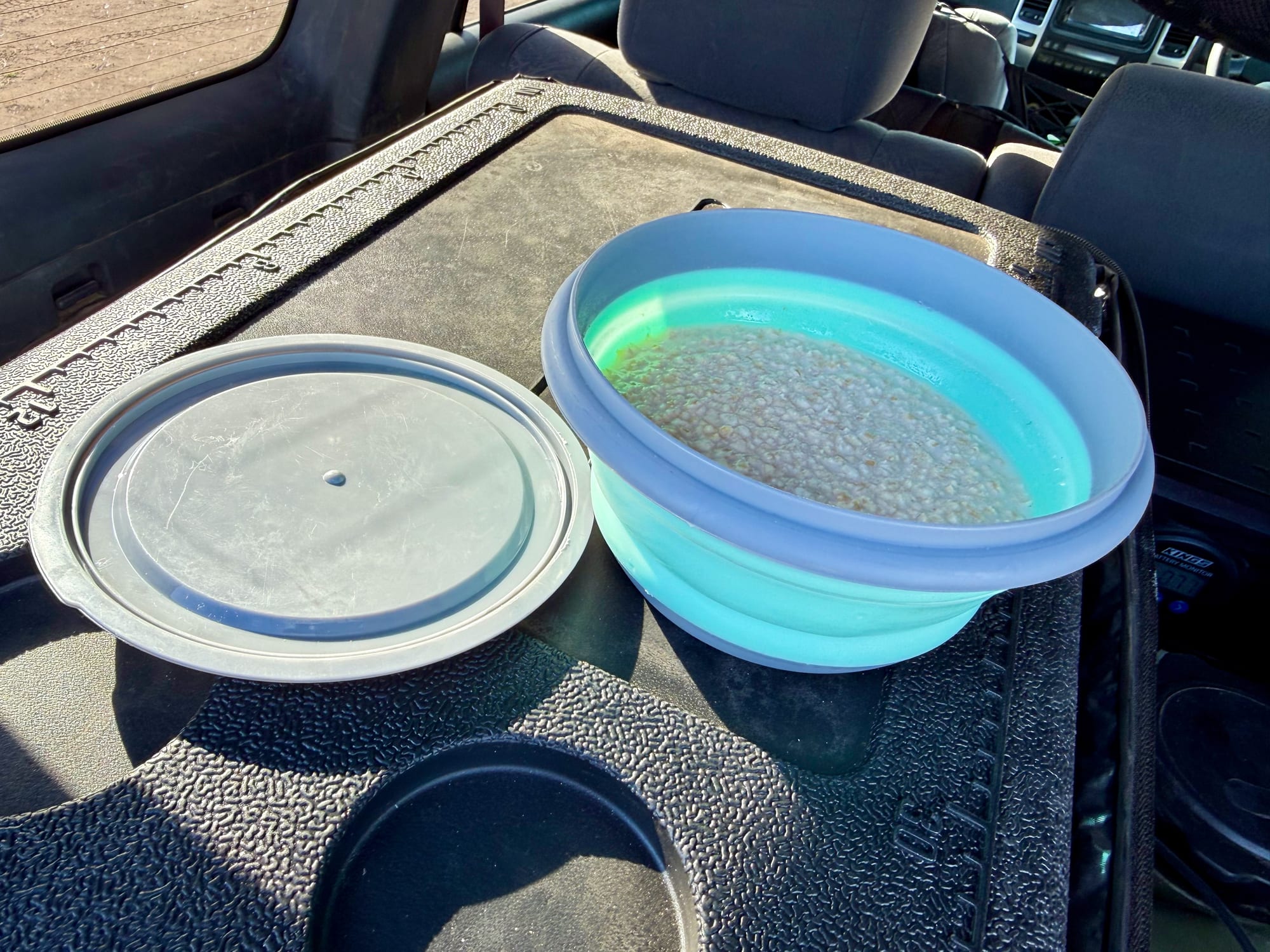 A silicone bowl with food in it next to its grey lid, on the back of a 4WD
