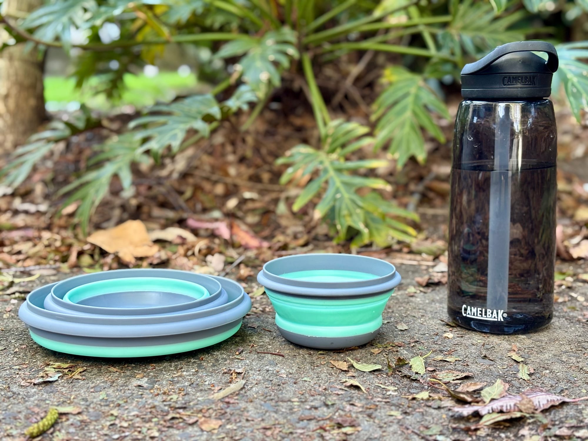 The nested silicone bowls folded flat and one bowl popped up, next to a 1 L CamelBak drink bottle for size