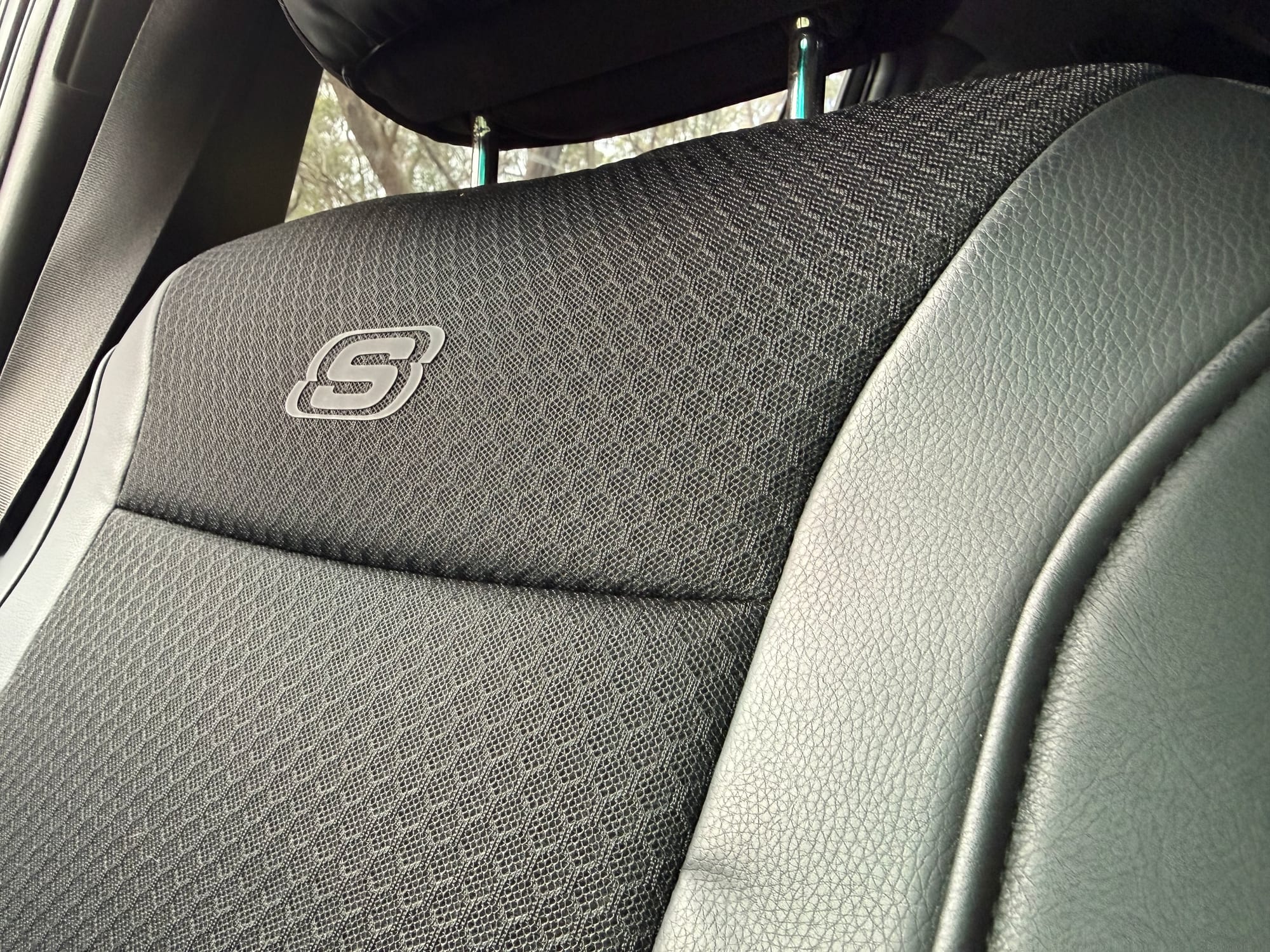 A close-up of the black mesh and leather-look panels of the Skechers seat cover with the S logo