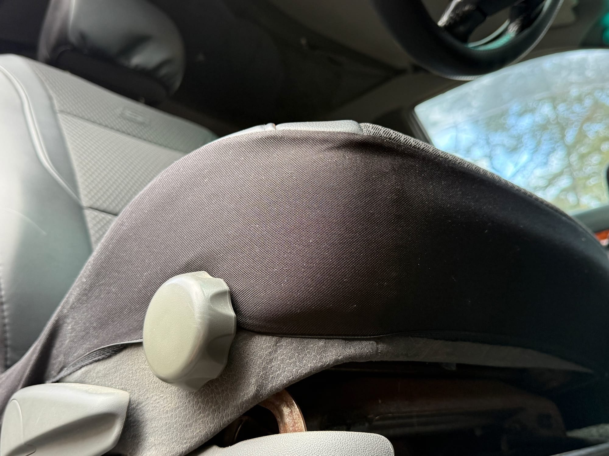 The stretch skirt of the Skechers seat cover wrapped around the front edge of the seat base, below the seat adjuster knob