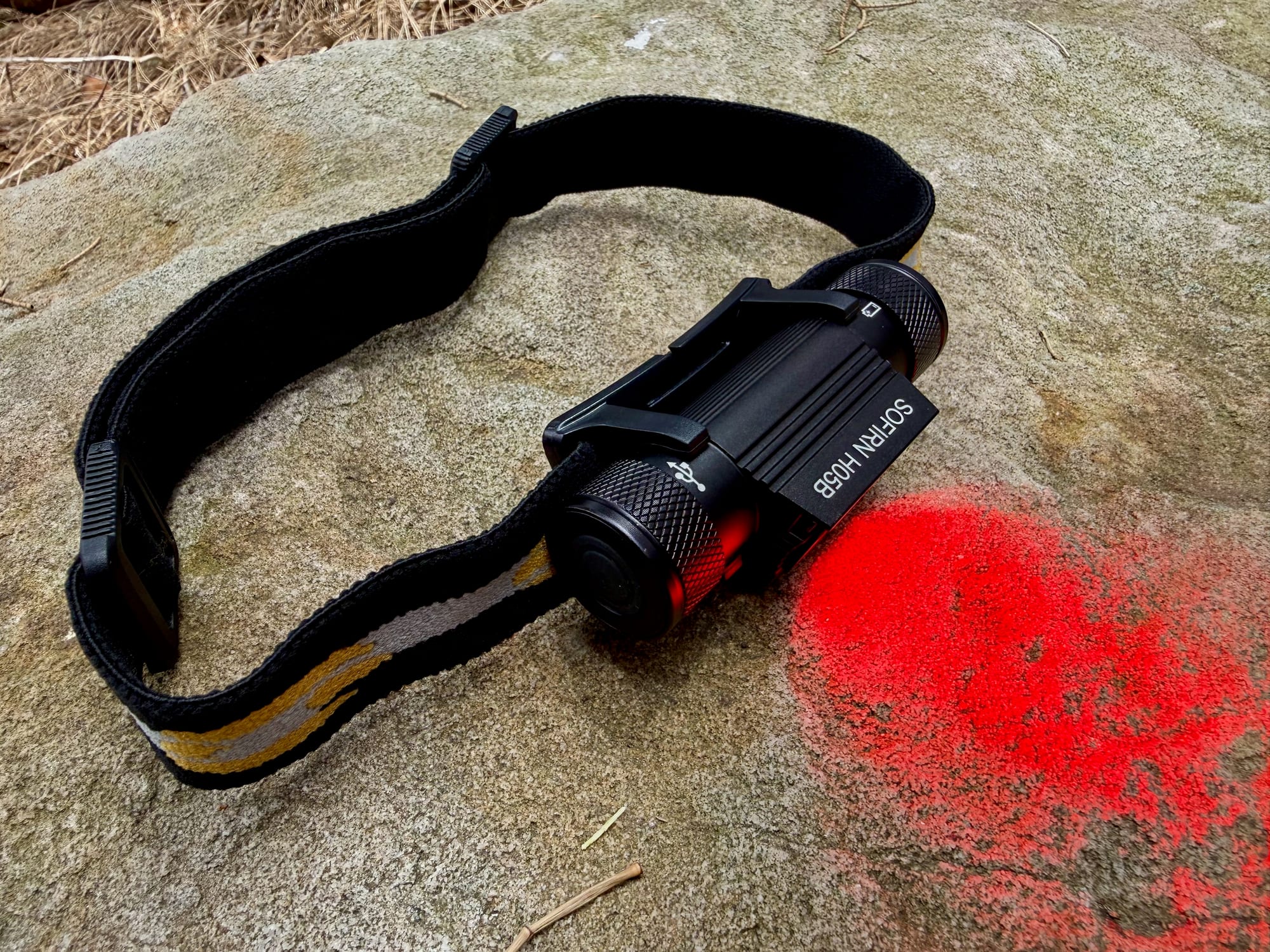 The red light of the Sofirn H05B headlamp shining on a rock
