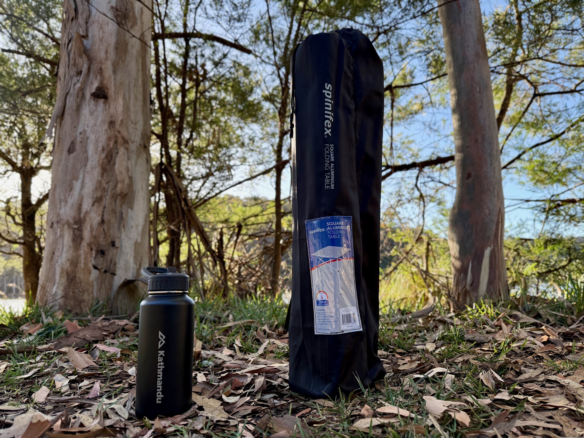 The Spinifex table packed in its black carry bag next to a drink bottle