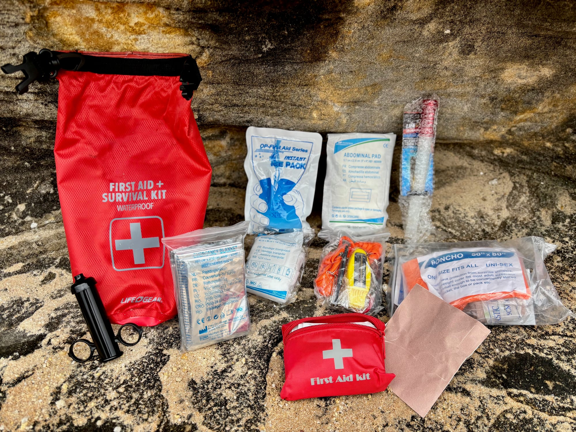 The contents of the first aid and survival kit laid out on a rock next to the red dry bag