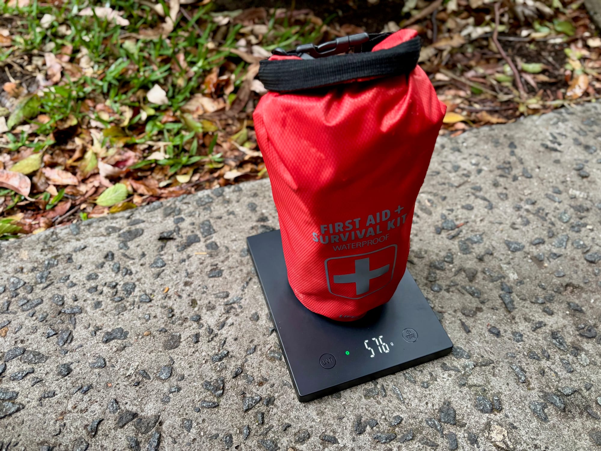 The red first aid and survival kit dry bag on a scale showing 576 g