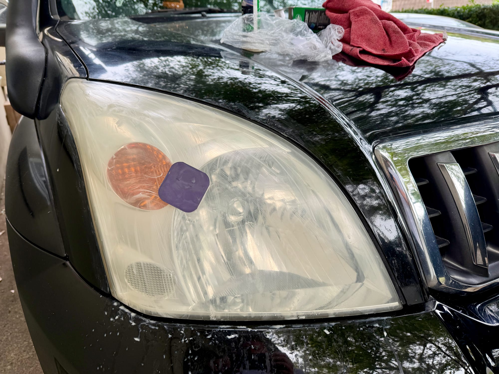 The purple pad sitting on the wet headlight lens during the last sanding stage