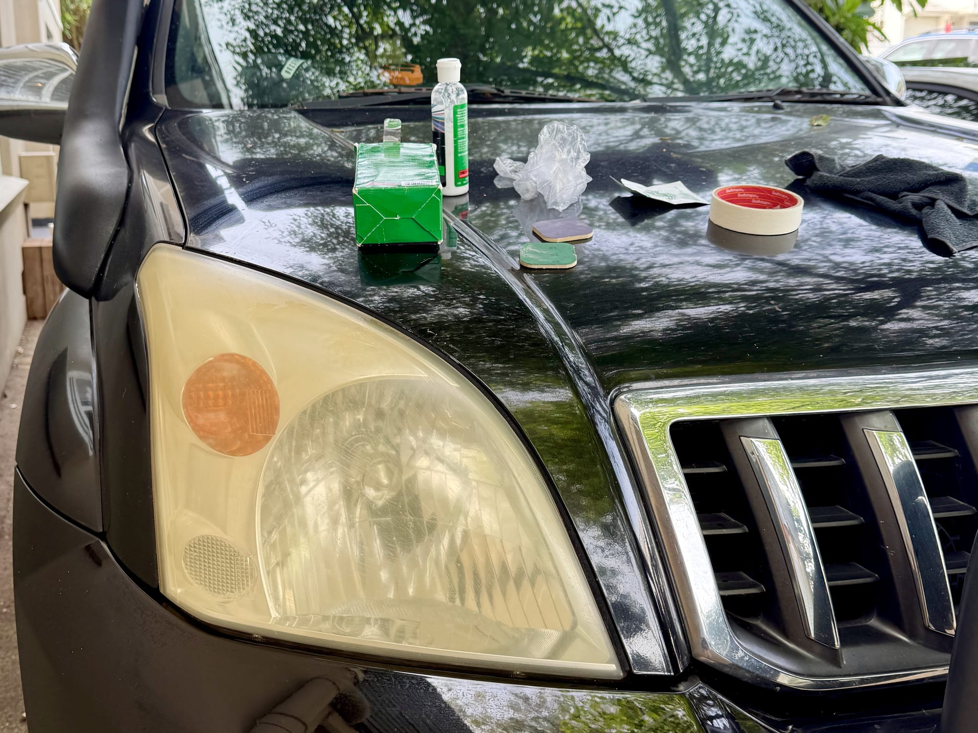A badly yellowed, cloudy headlight on a black 4WD, with the Turtle Wax kit laid out on the bonnet