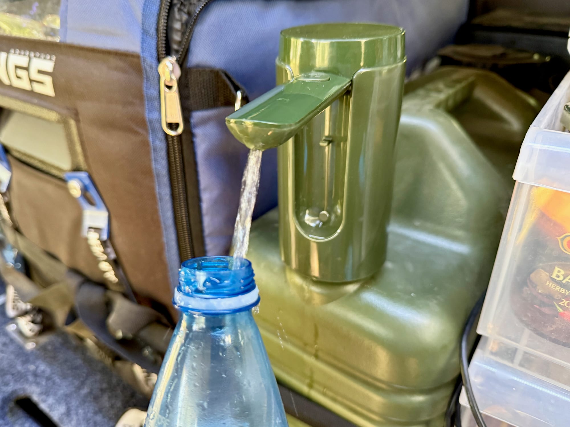 The pump filling a water bottle from the container in the back of a 4WD