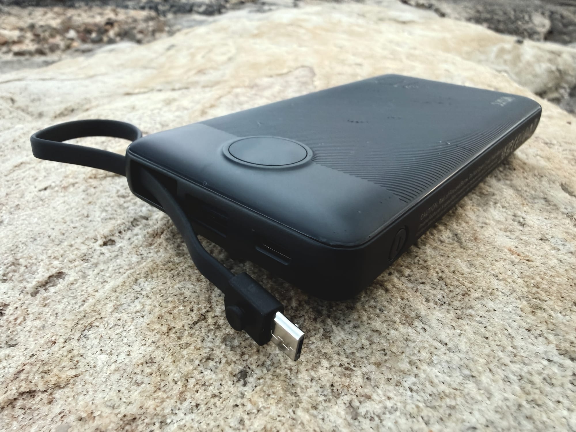 The Micro-USB cable of the VRURC power bank pulled out of the side, where it forms the carry loop
