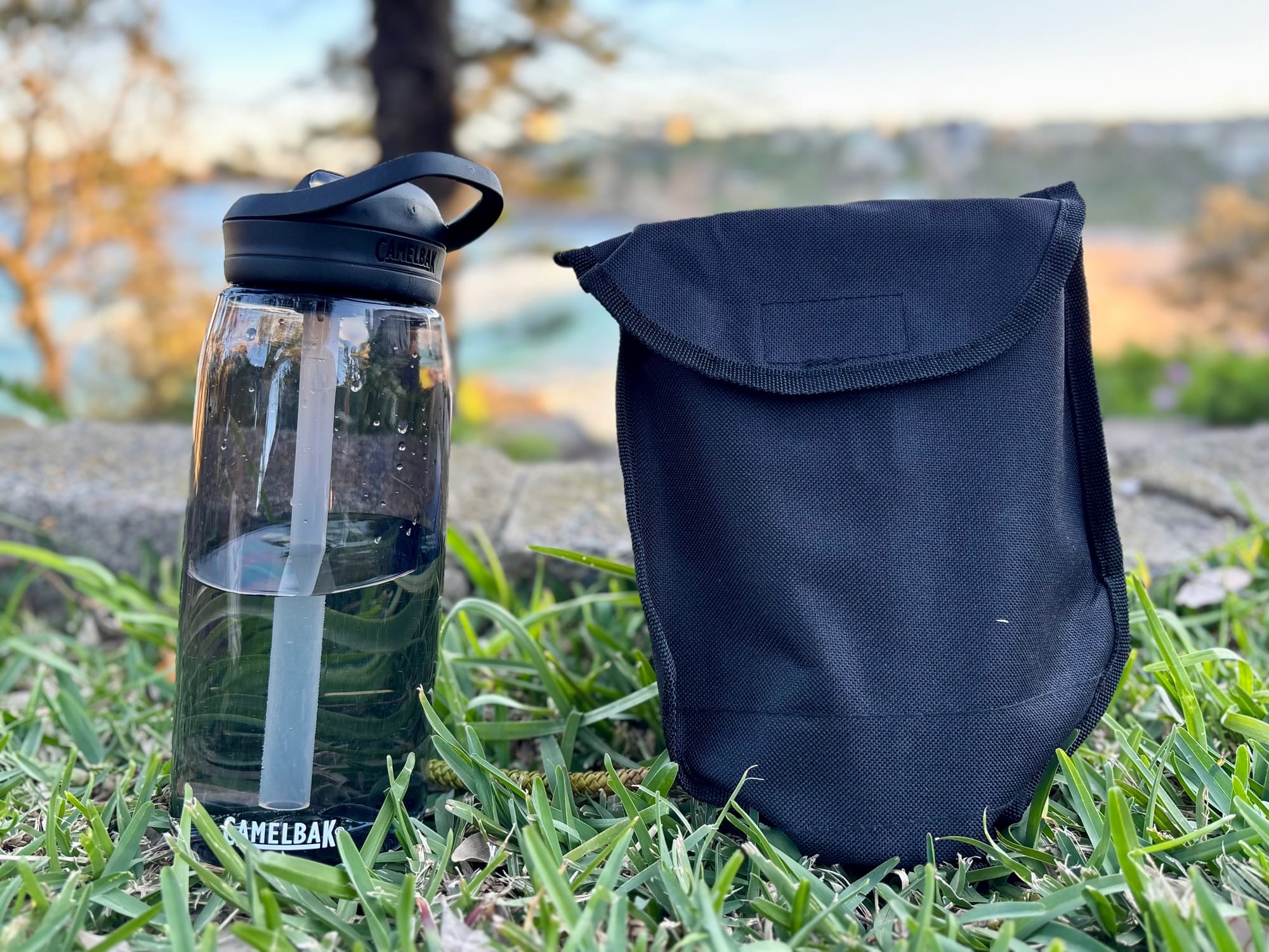The shovel in its black pouch standing next to a CamelBak water bottle