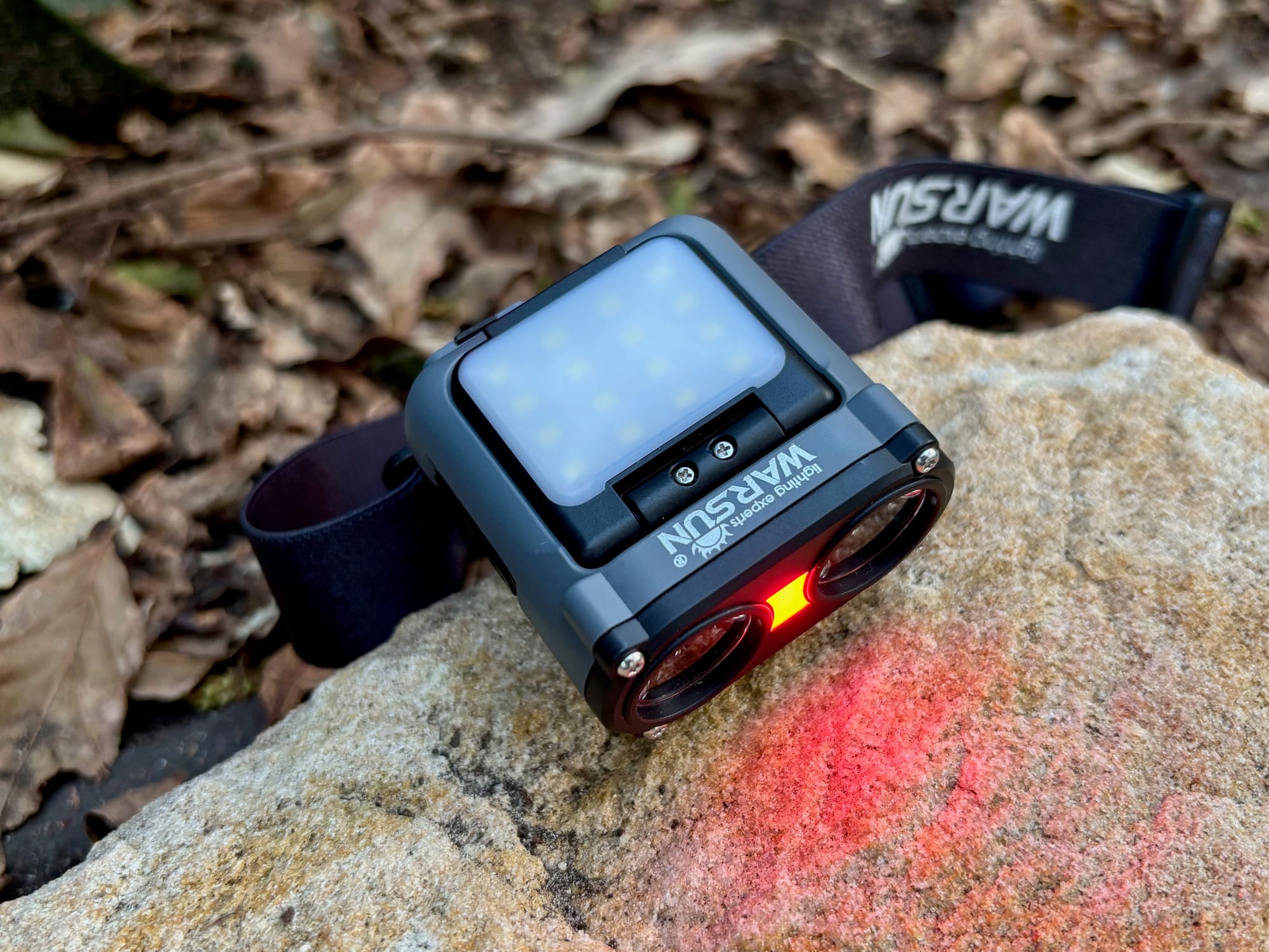 The Warsun headlamp on a rock with its red warning light on between the two spotlights