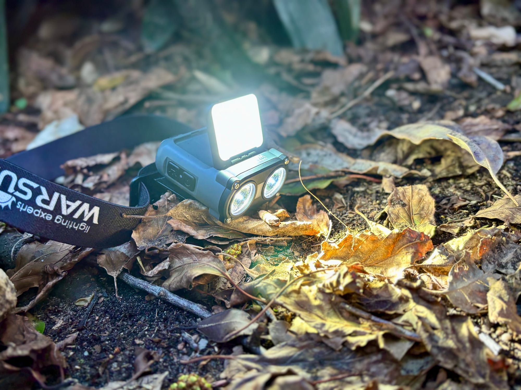 The Warsun headlamp lying on autumn leaves with its two spotlights and its flip-up panel light switched on