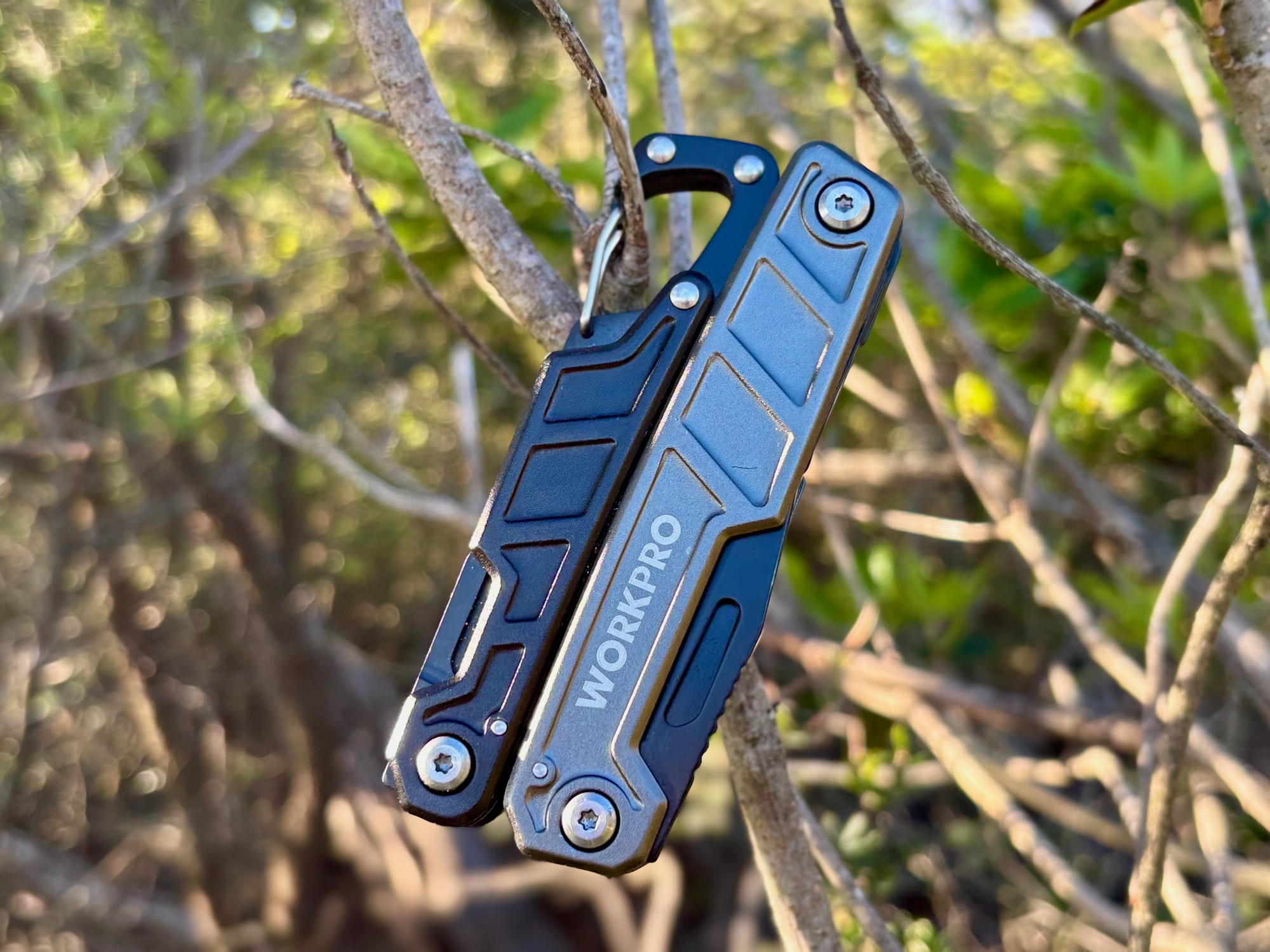 The Workpro 11-in-1 multitool hanging from a thin branch by its built-in carabiner