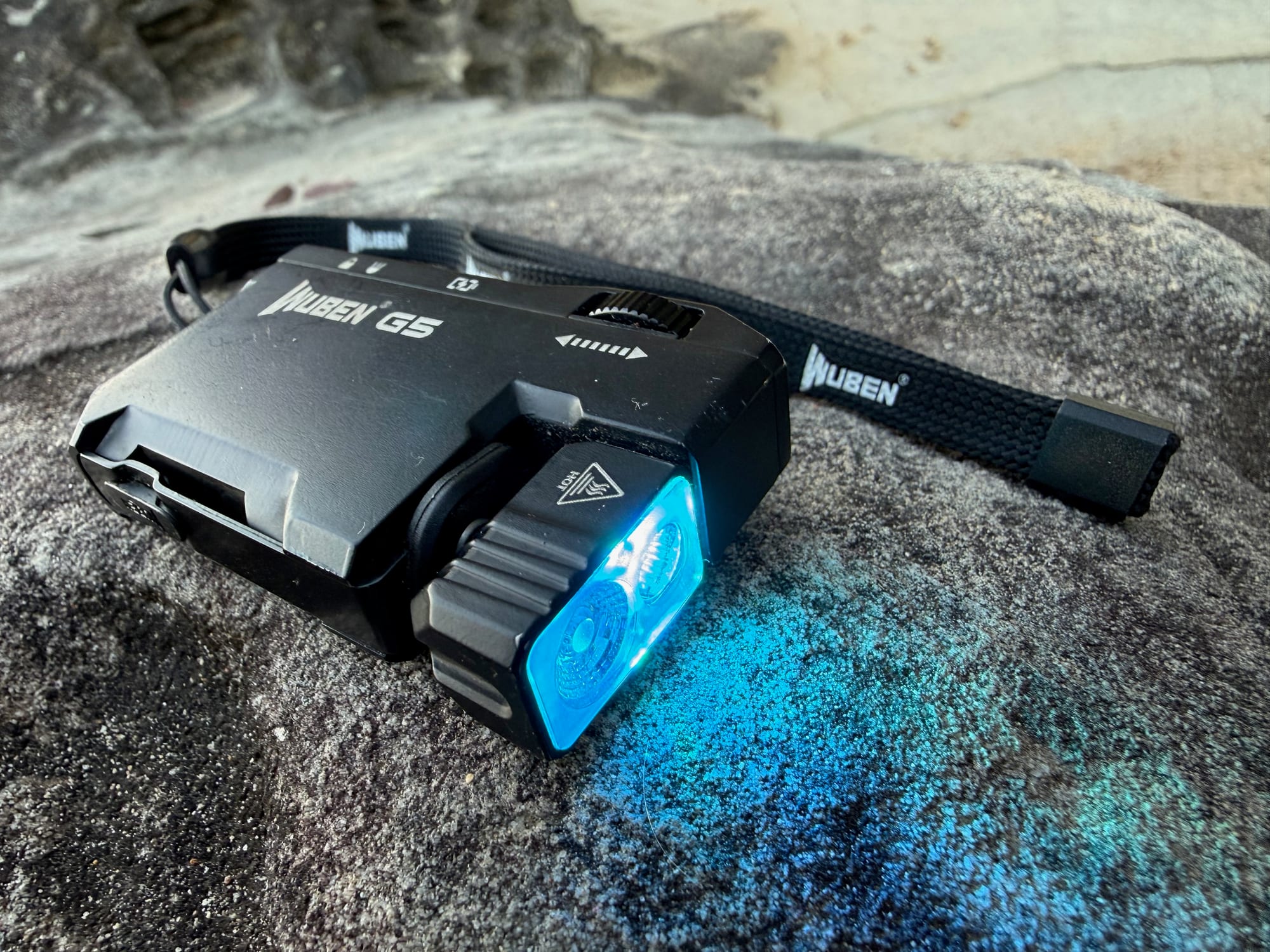 The Wuben G5 lying on a rock, throwing cyan light onto the stone