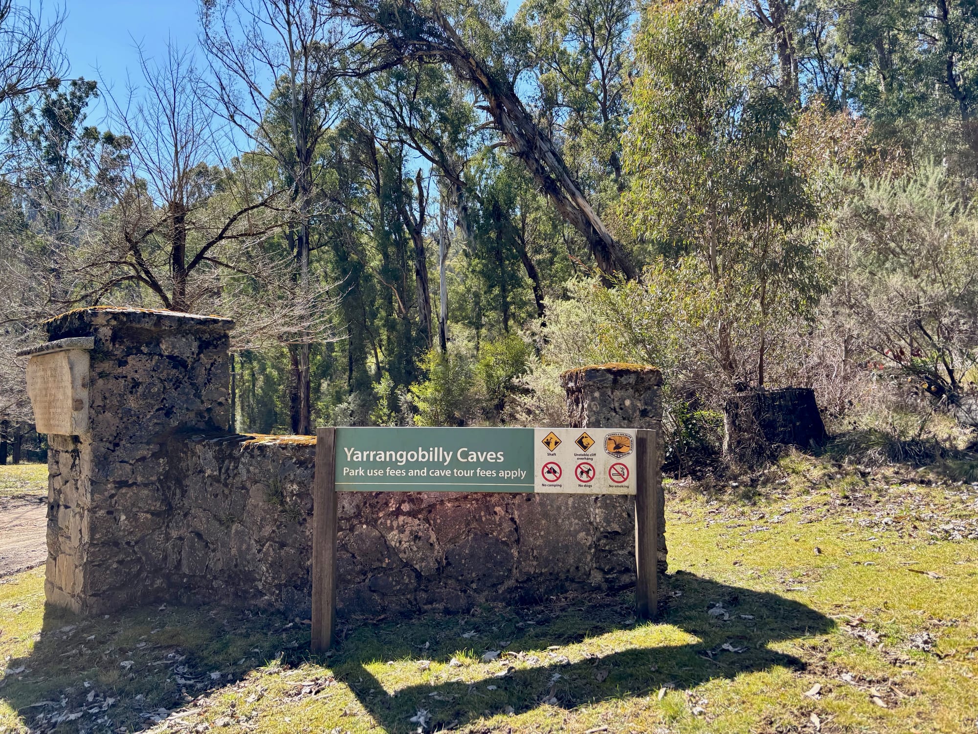 The stone gateway at Yarrangobilly Caves with the sign saying park use fees and cave tour fees apply
